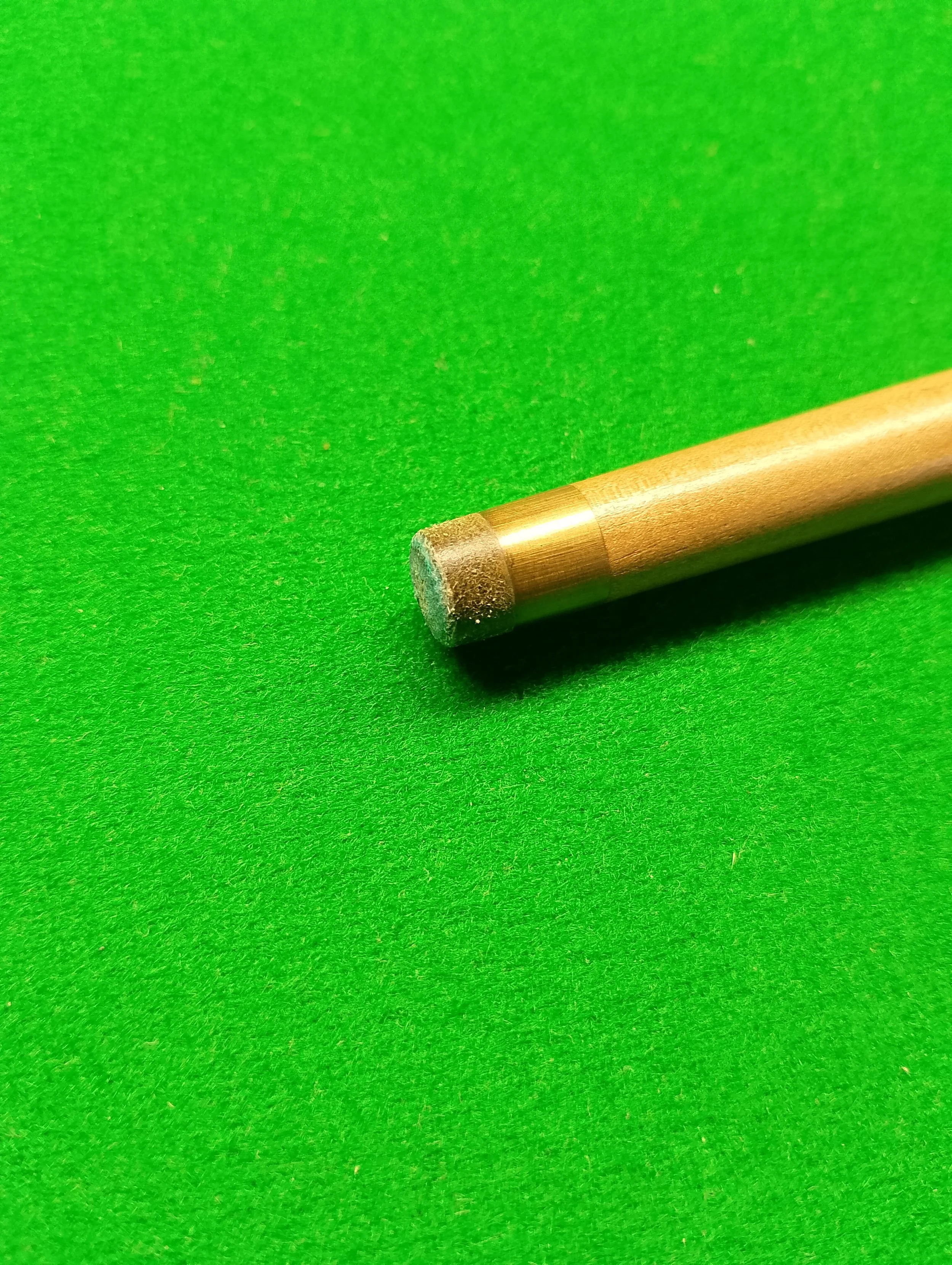 Close-up of a metallic cue tip on a snooker or pool cue resting on a green felt pool table.