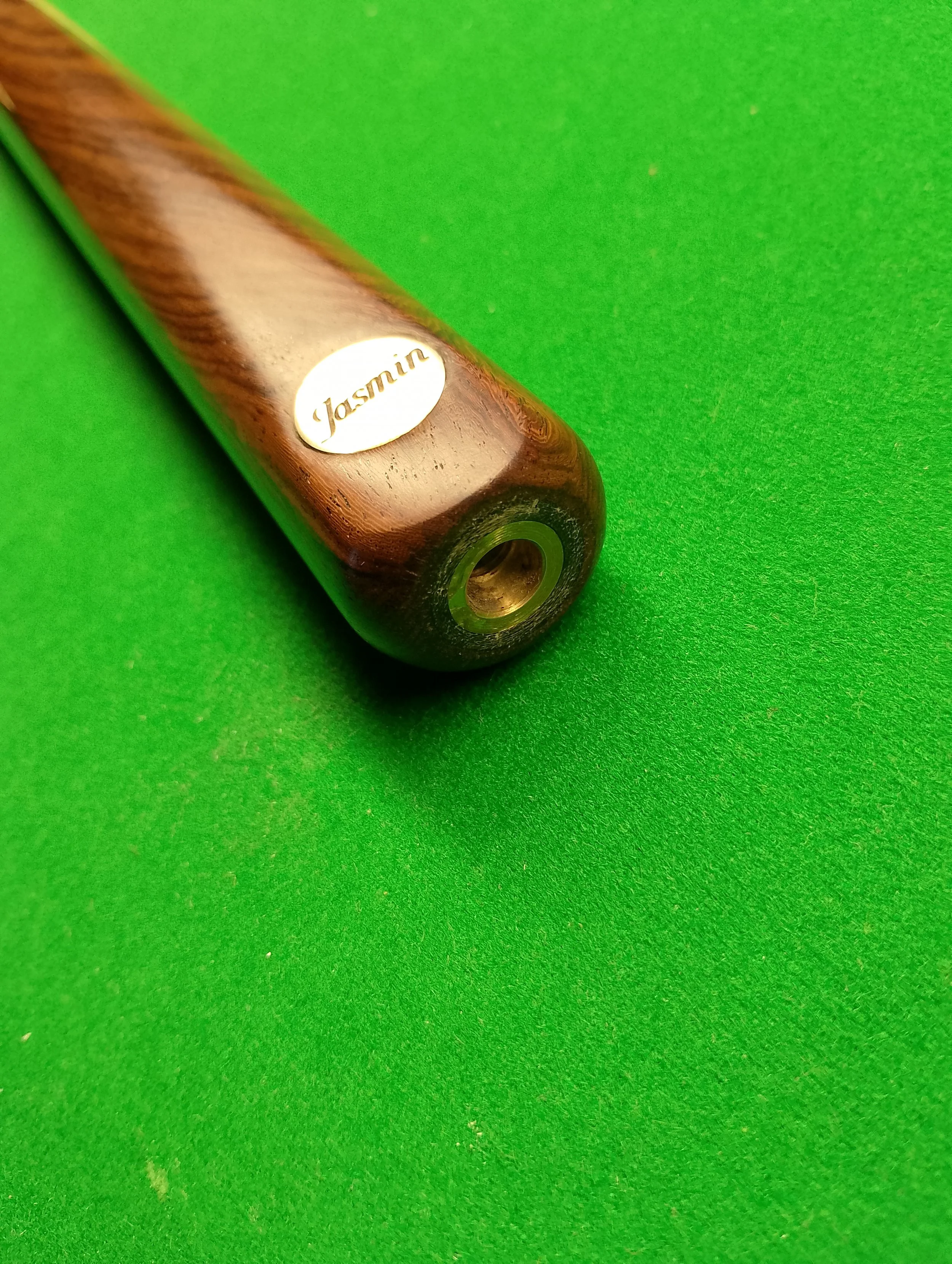 Close-up of a wooden cue stick with a sticker labeled 'Jasmin' on a green billiard table.