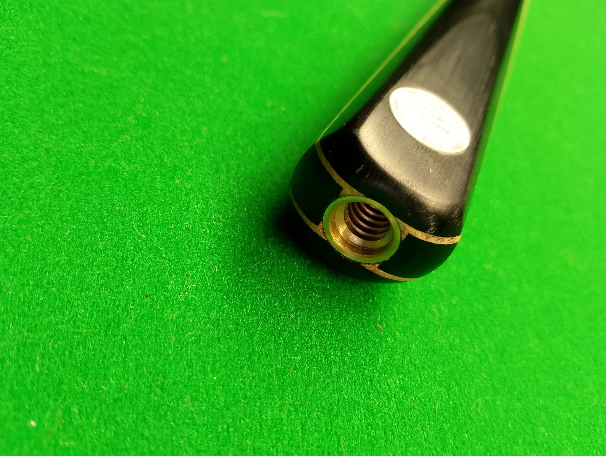 Close-up of a part of a black device on a green surface, showing a threaded hole at the end.