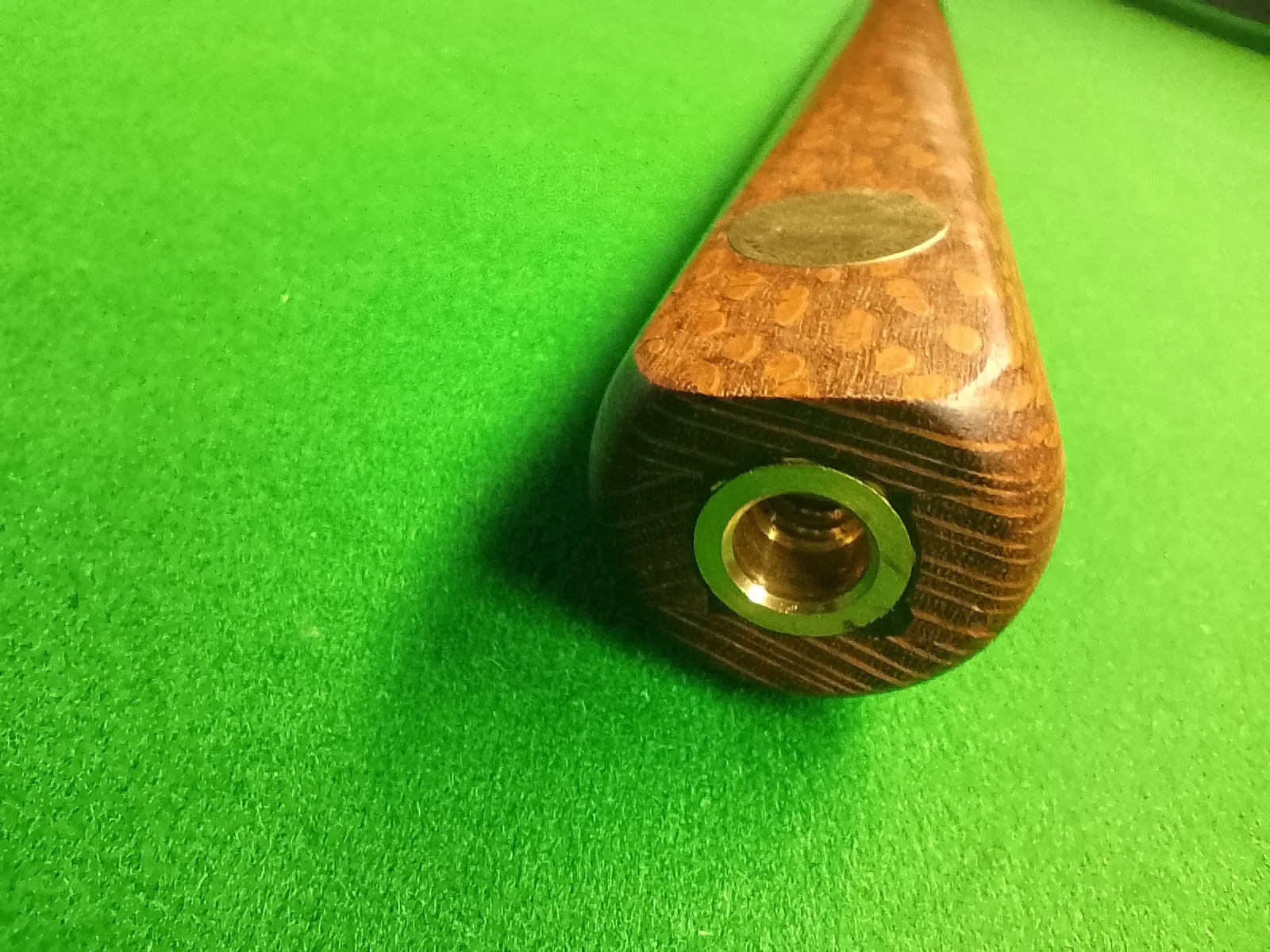 Wooden cue stick tip with a metal insert on a green felt surface.