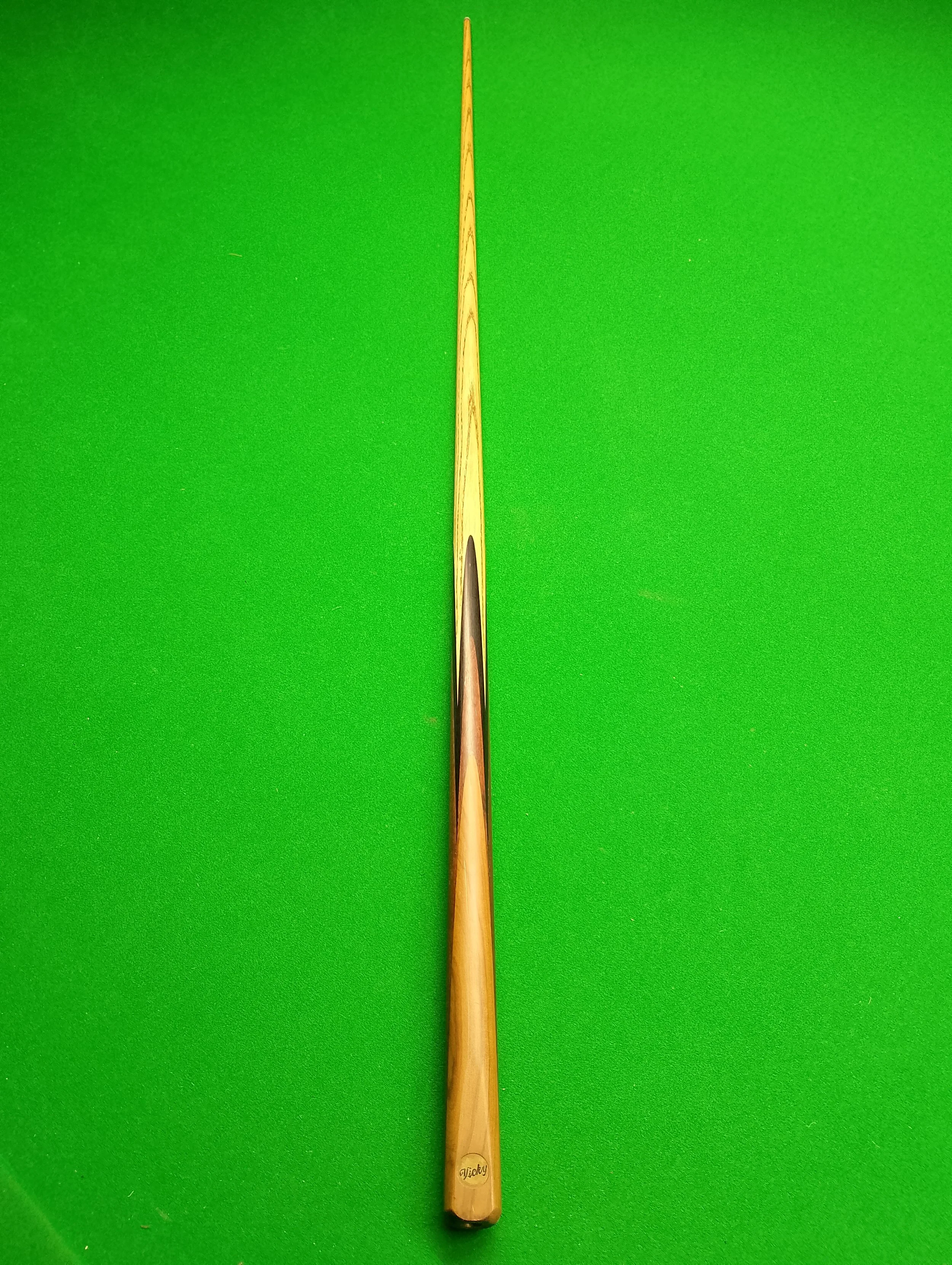 A wooden cue stick used for playing billiards or pool, placed vertically on a green felt table.