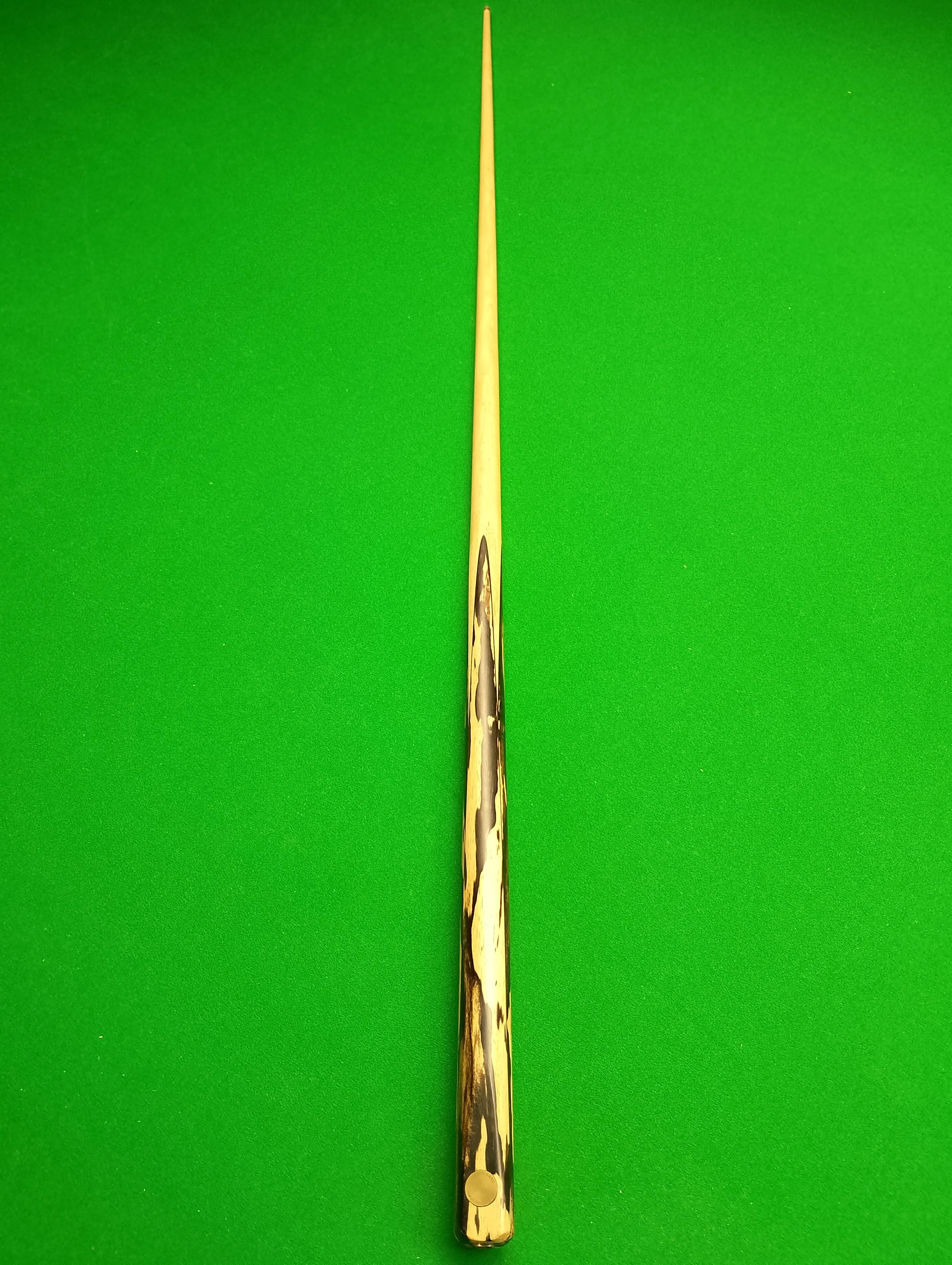 A single snooker cue stick lying on a green pool table.