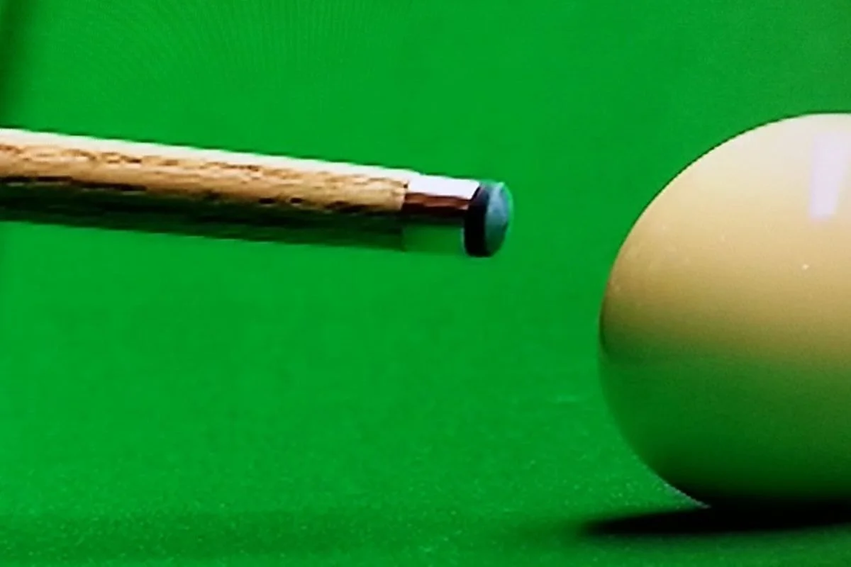 A snooker cue pointed at a snooker ball on a green snooker table.