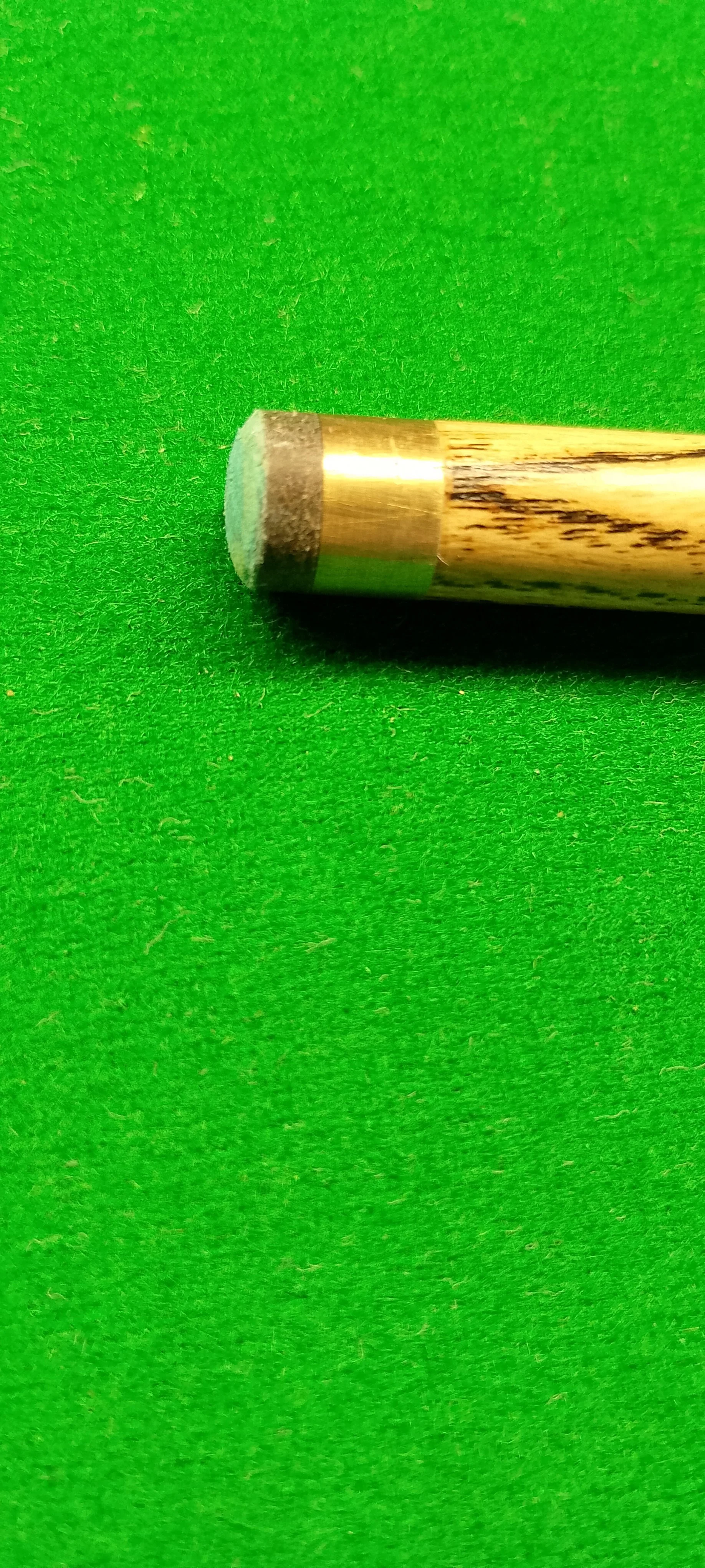 Close-up of a pool cue tip and shaft on a green felt pool table.