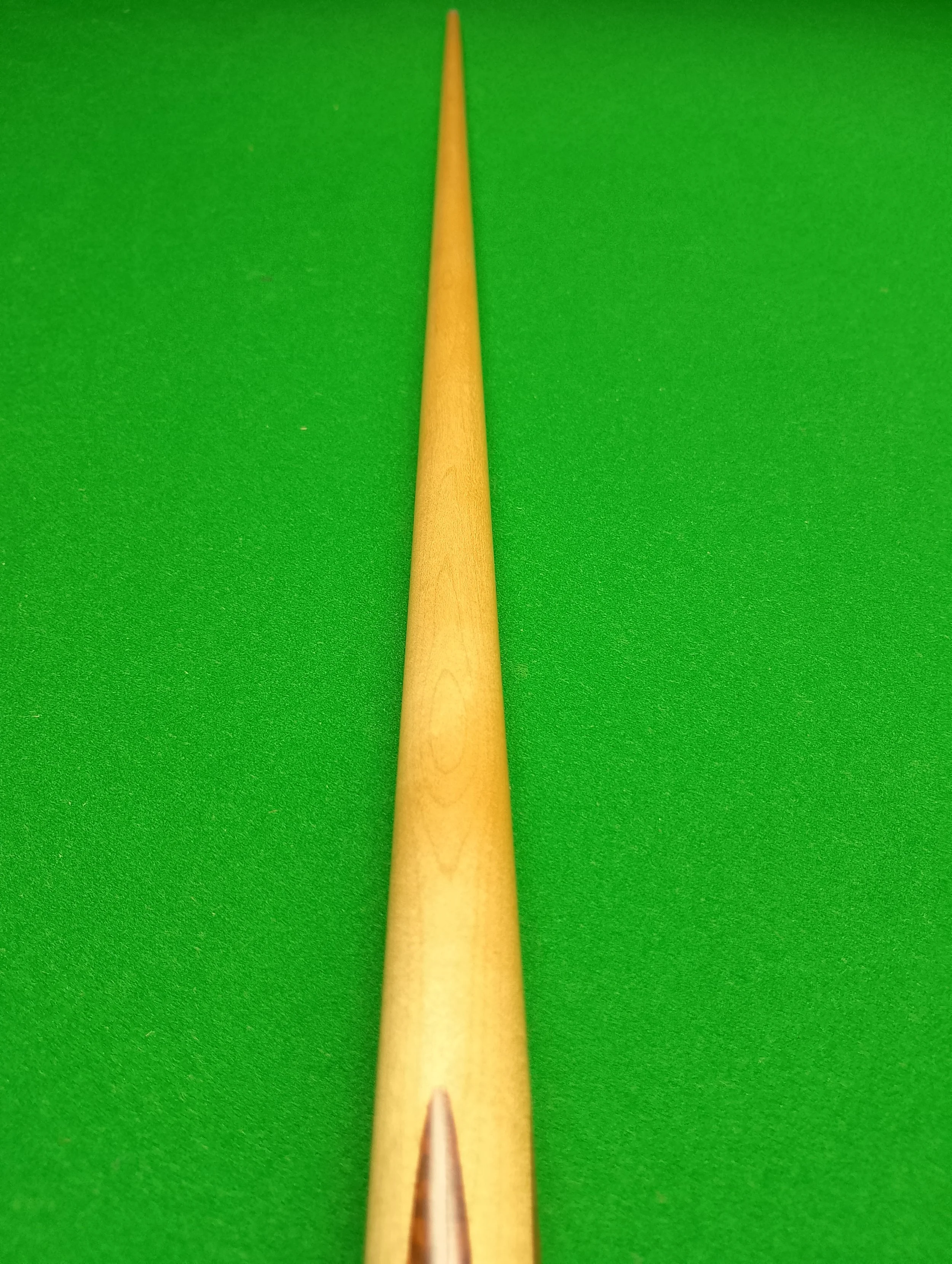 Close-up of a wooden cue stick on a green billiards or pool table surface.