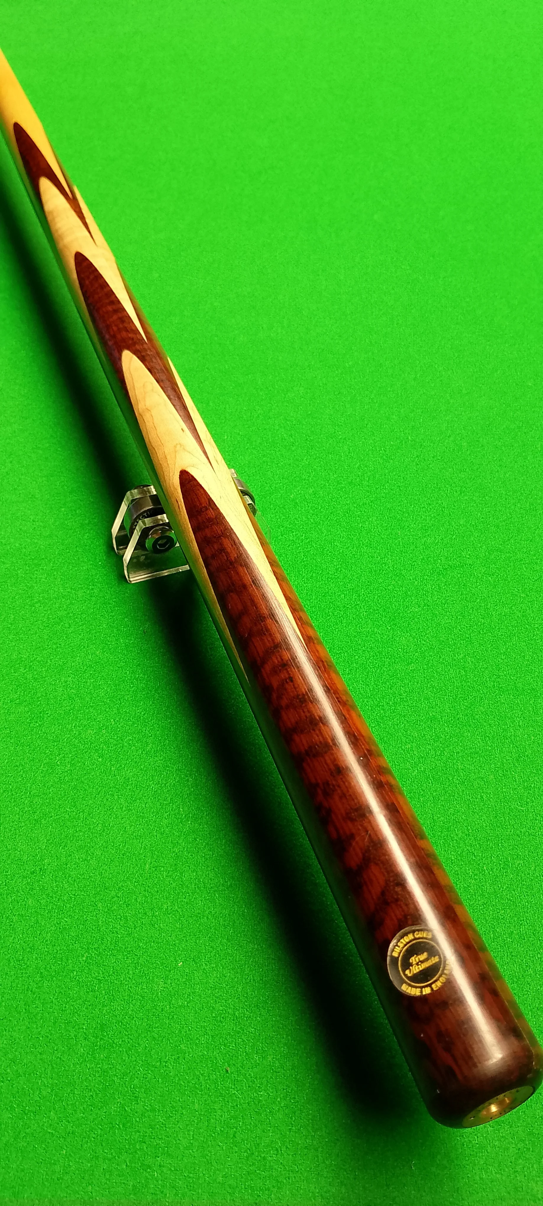 A wooden pool cue resting on a cue stand on a green pool table surface.