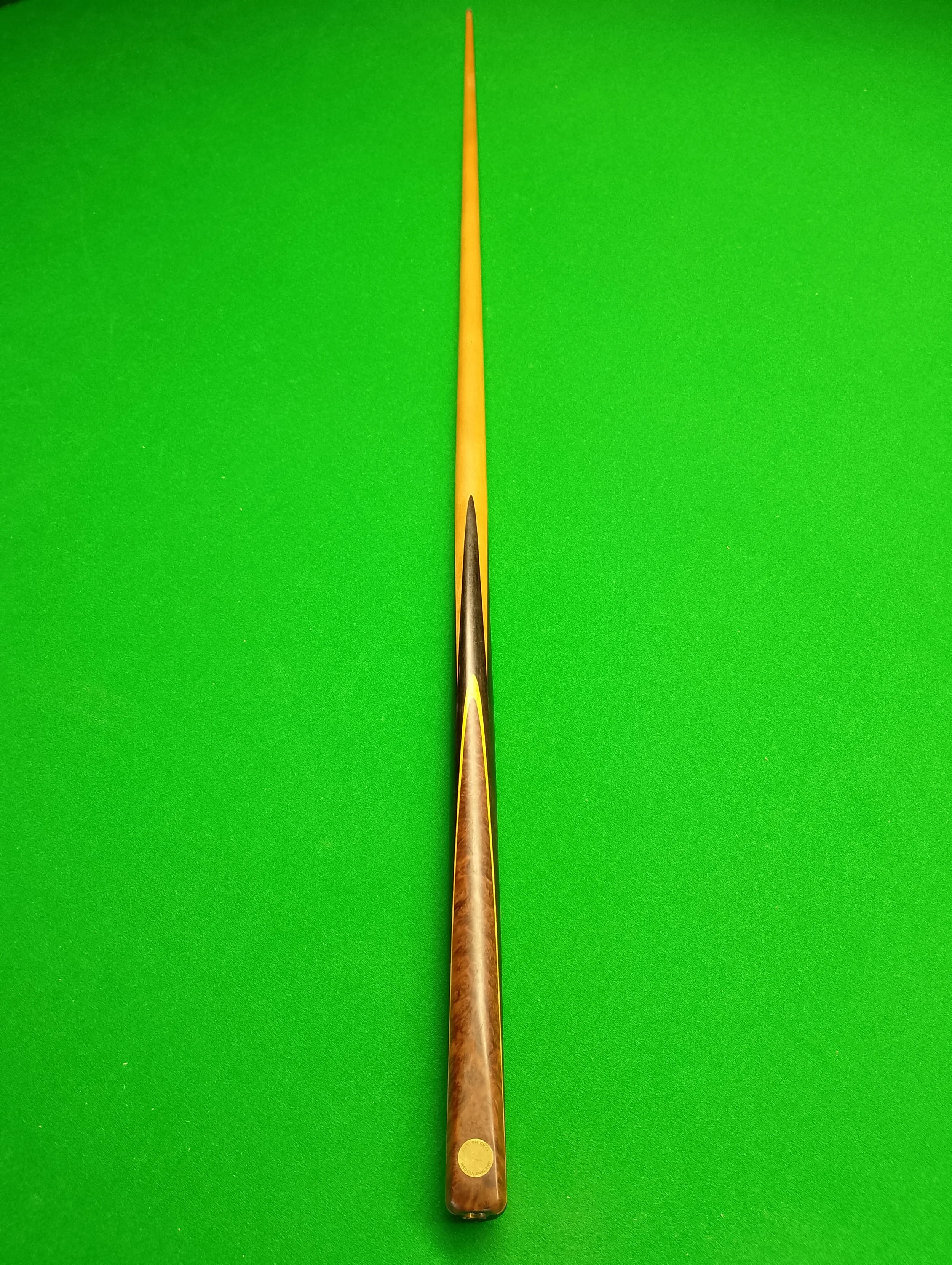 A long, slim pool cue stick with a wooden finish, placed vertically on a green billiard table.