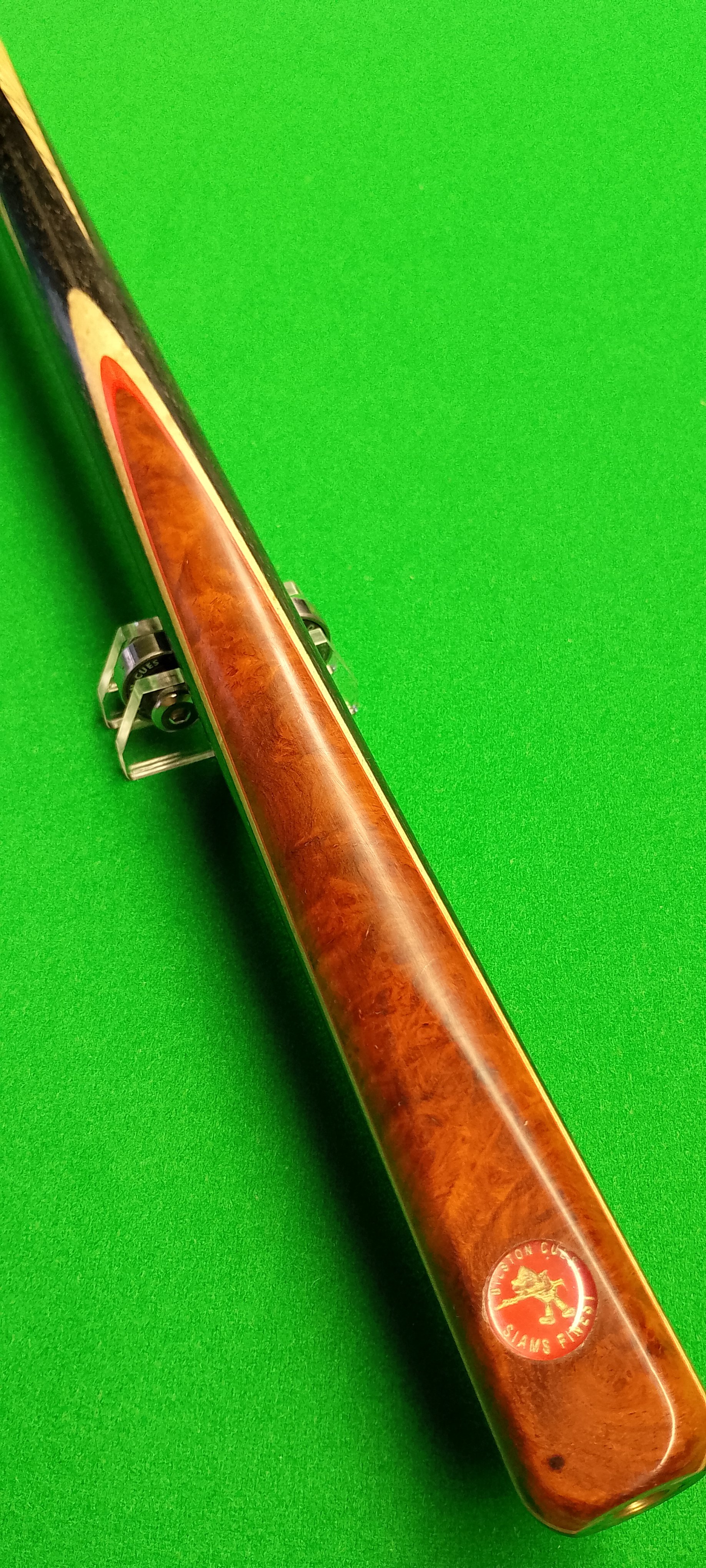 Close-up of a wooden pool cue with a logo at the bottom, resting on a green felt pool table.