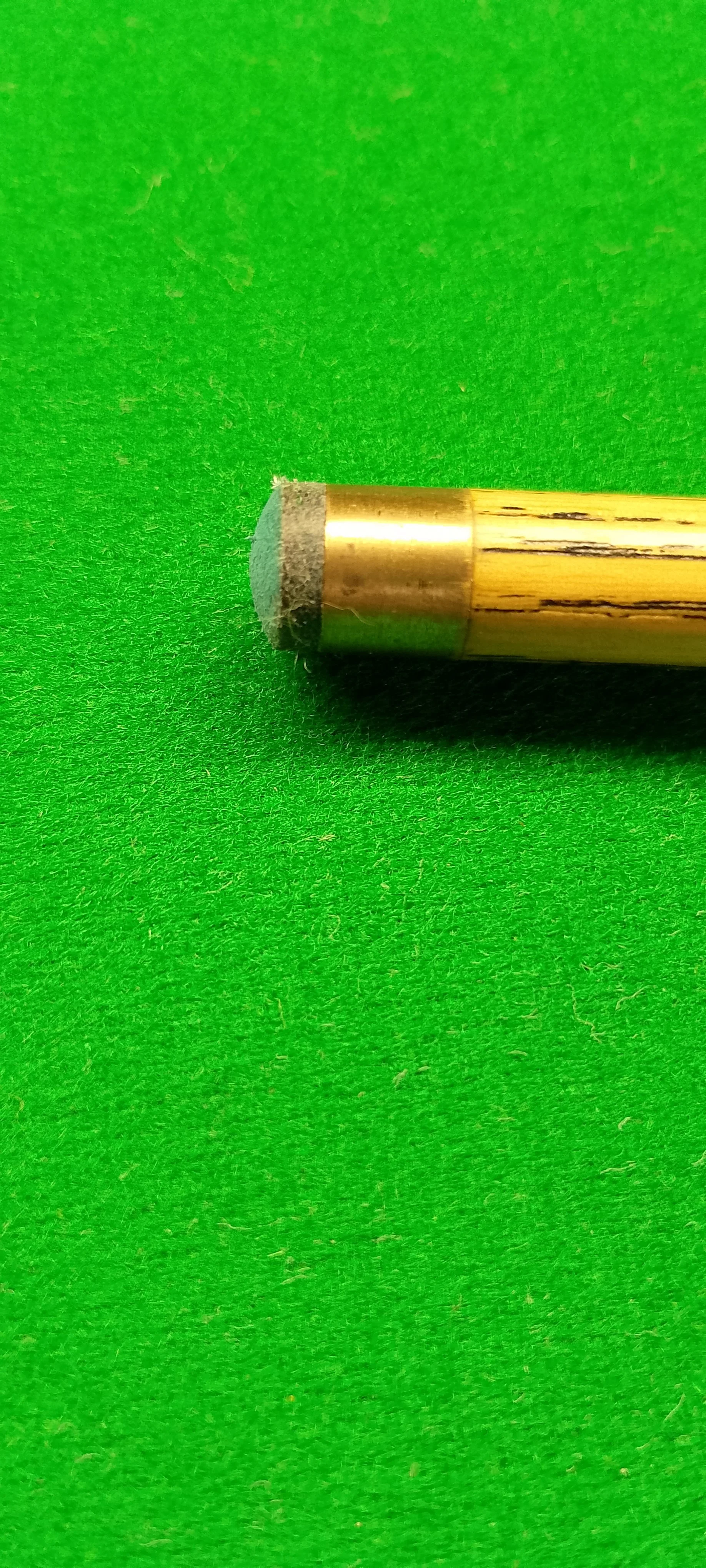 Close-up of a metallic mechanical part with a cylindrical shape on a bright green fabric background.