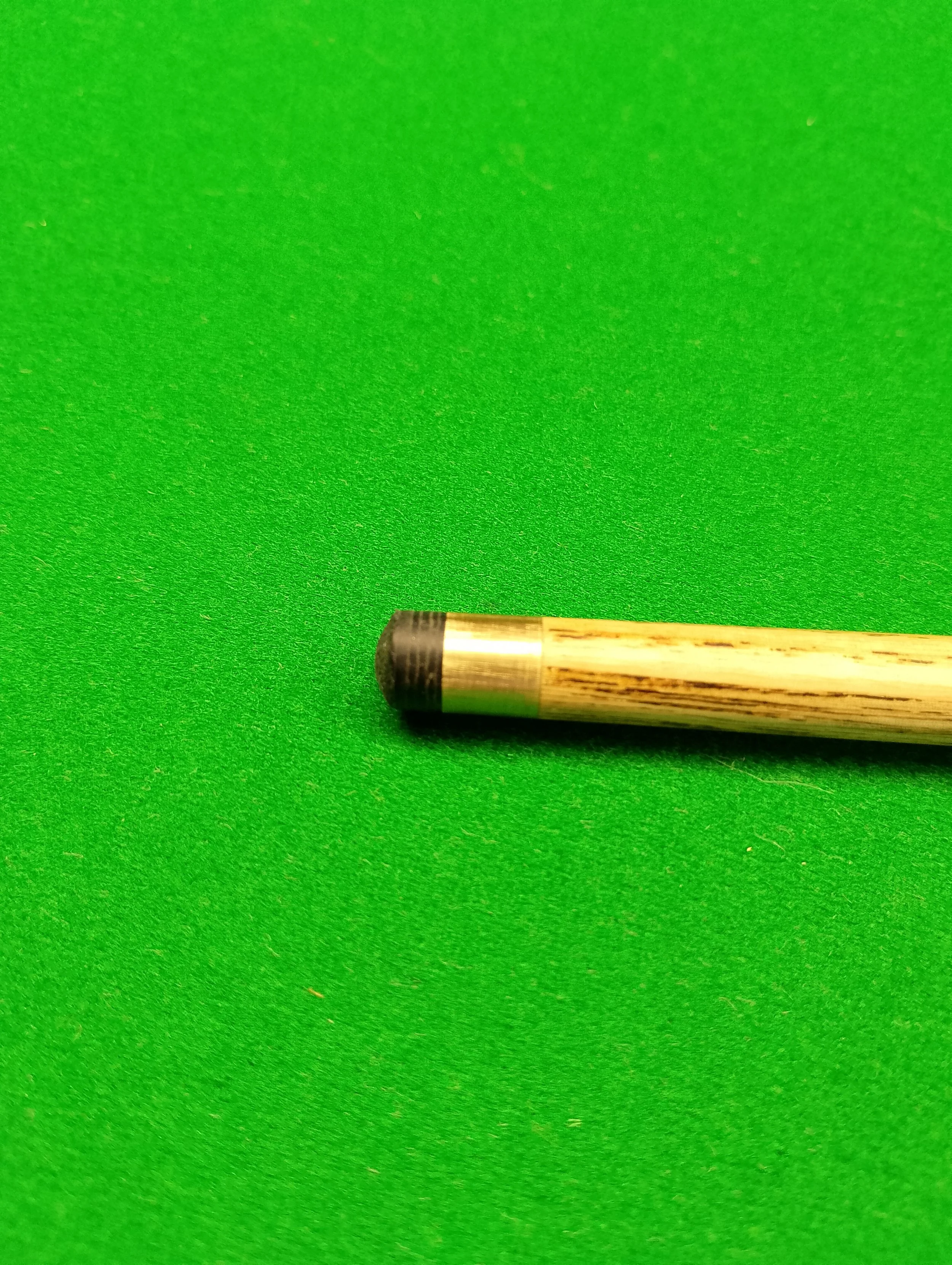 Close-up of a pool cue stick on green felt surface.