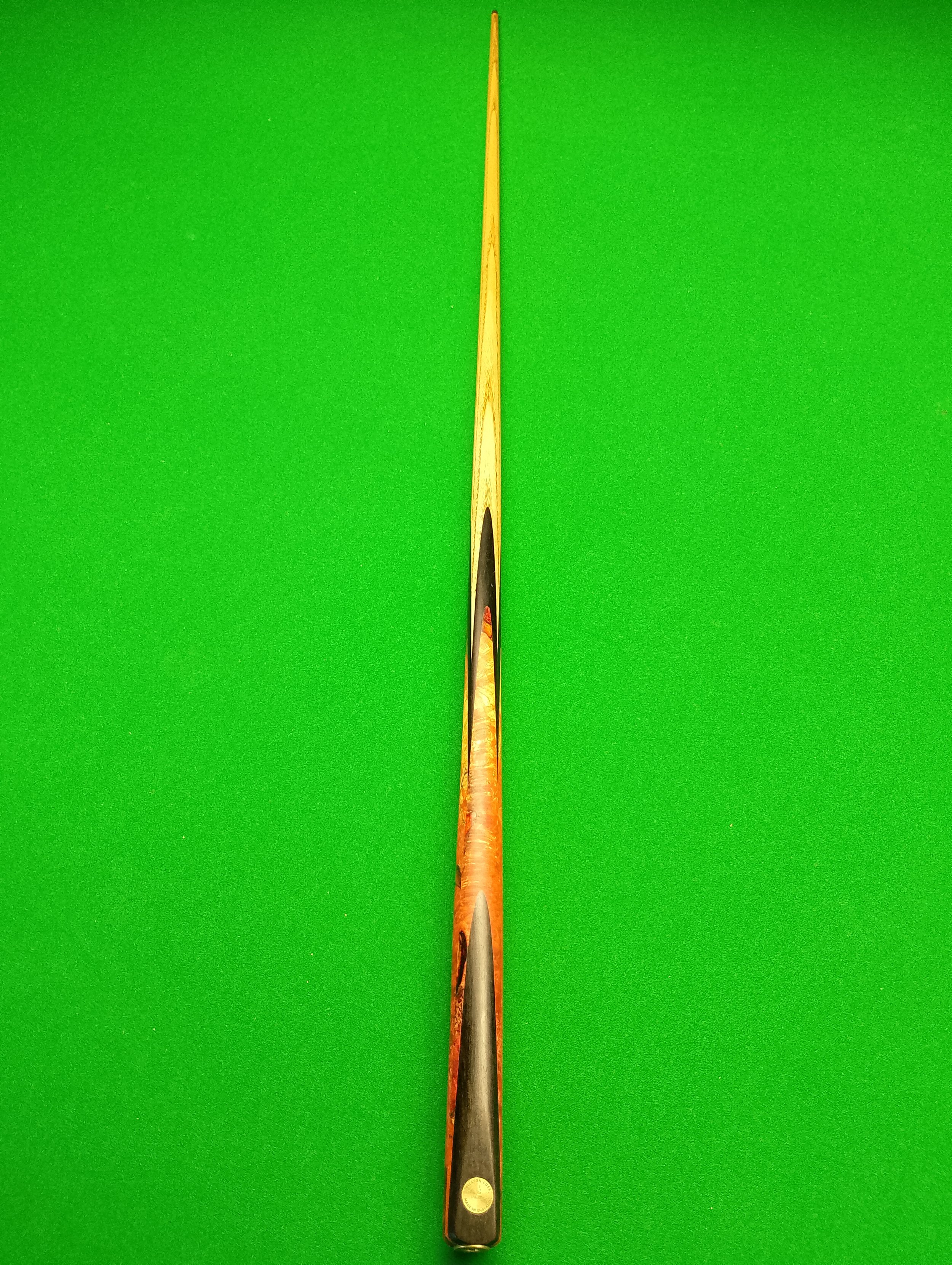 A pool cue with a decorative design on the handle, placed vertically on a bright green pool table surface.