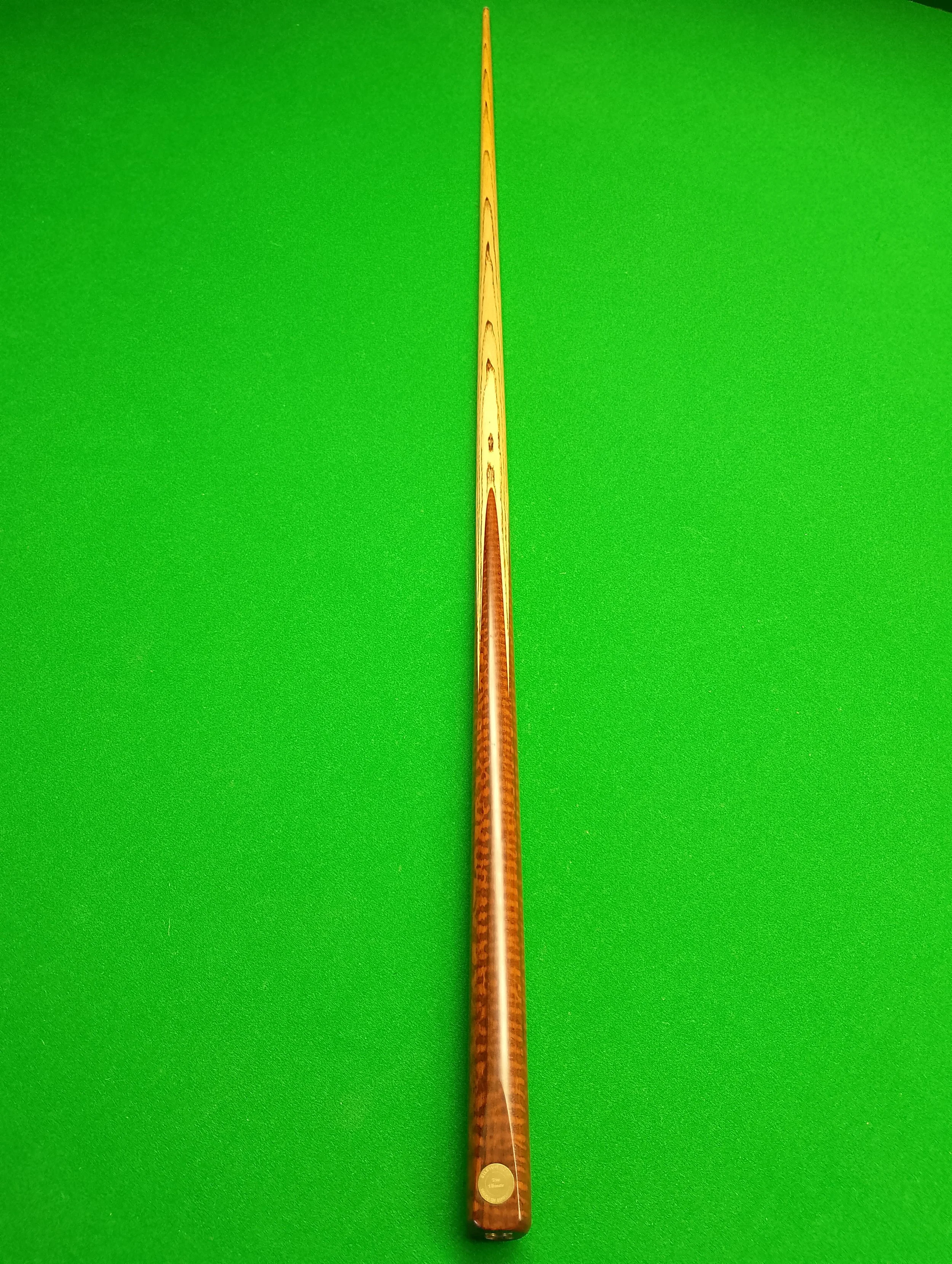 A wooden snooker cue resting on a green pool table.