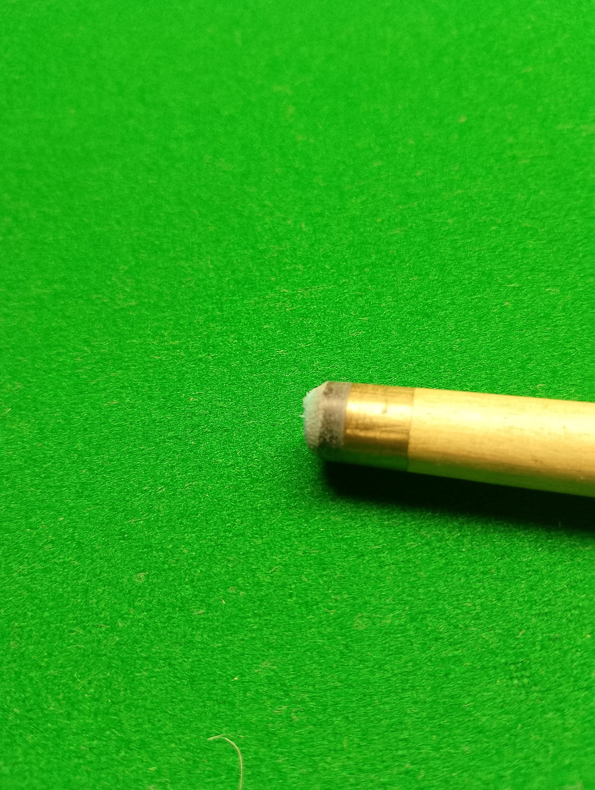 Close-up of a cue stick tip on a green pool table.