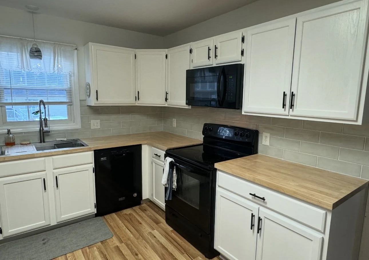 Kitchen with white cabinets, black appliances, wood countertops, a window above the sink, a small beige tile backsplash, and hardwood flooring.
