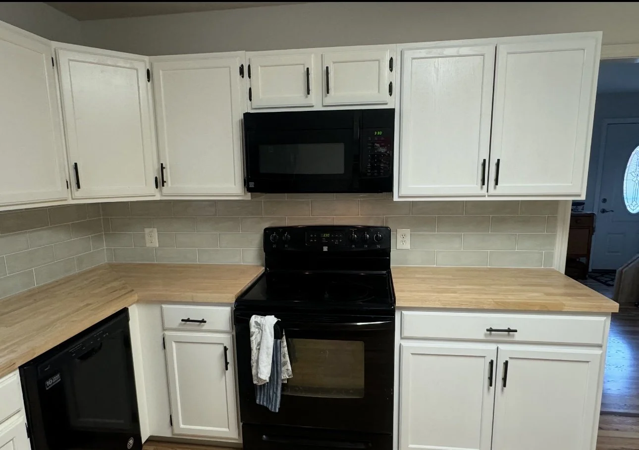 Kitchen with white cabinets, black appliances, and a beige tile backsplash.