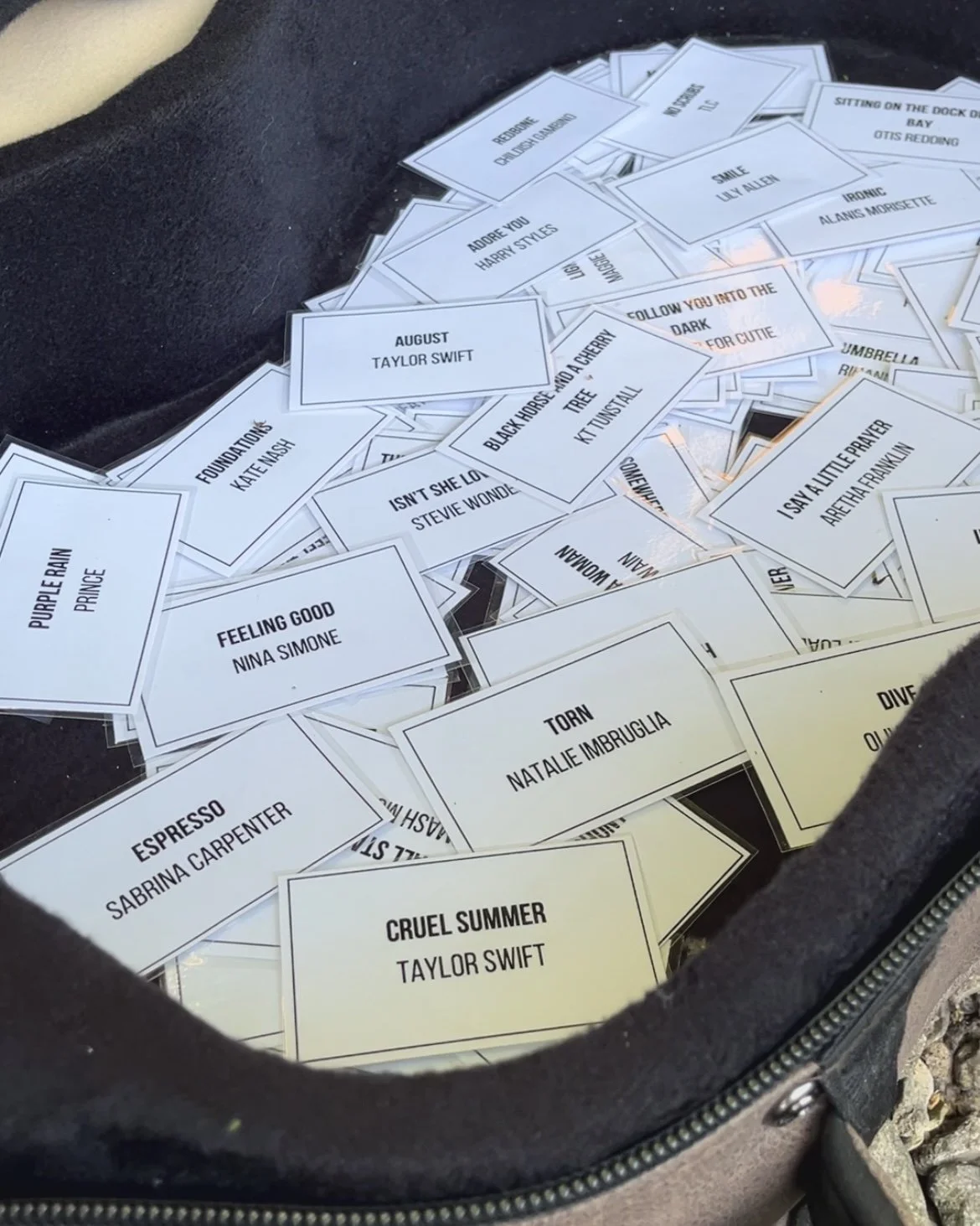 A collection of white cards with song titles and artists, scattered inside a guitar case.