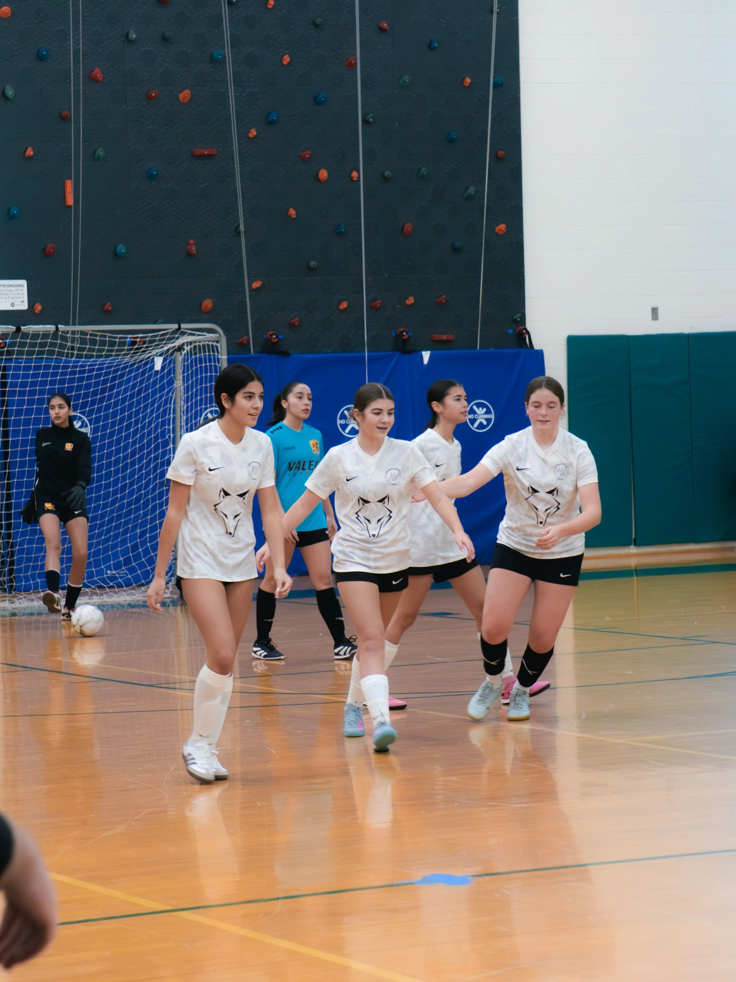 Women’s indoor soccer team celebrating on the court with a rock climbing wall in the background.
