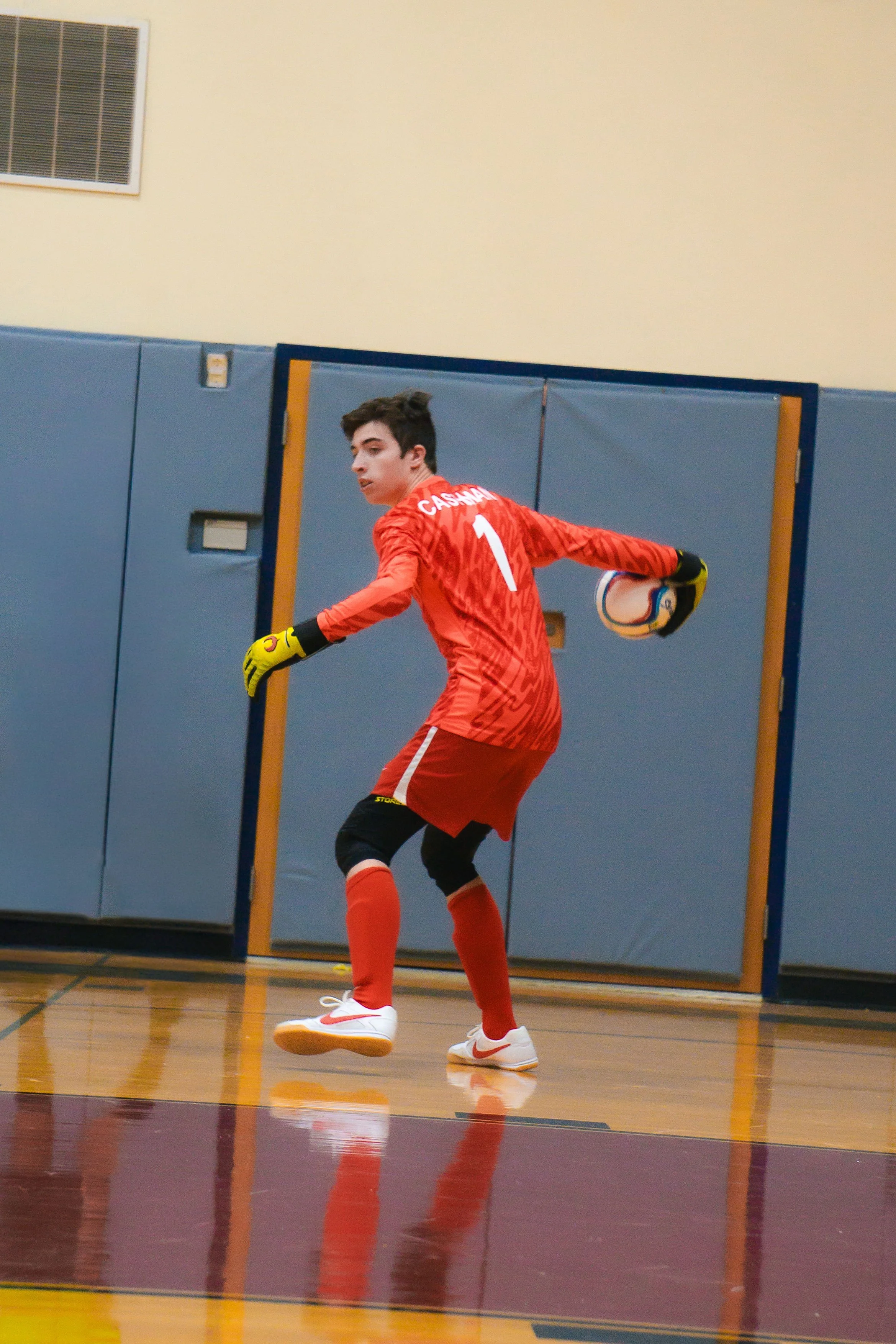 Young male goalkeeper in red uniform making a save in indoor soccer