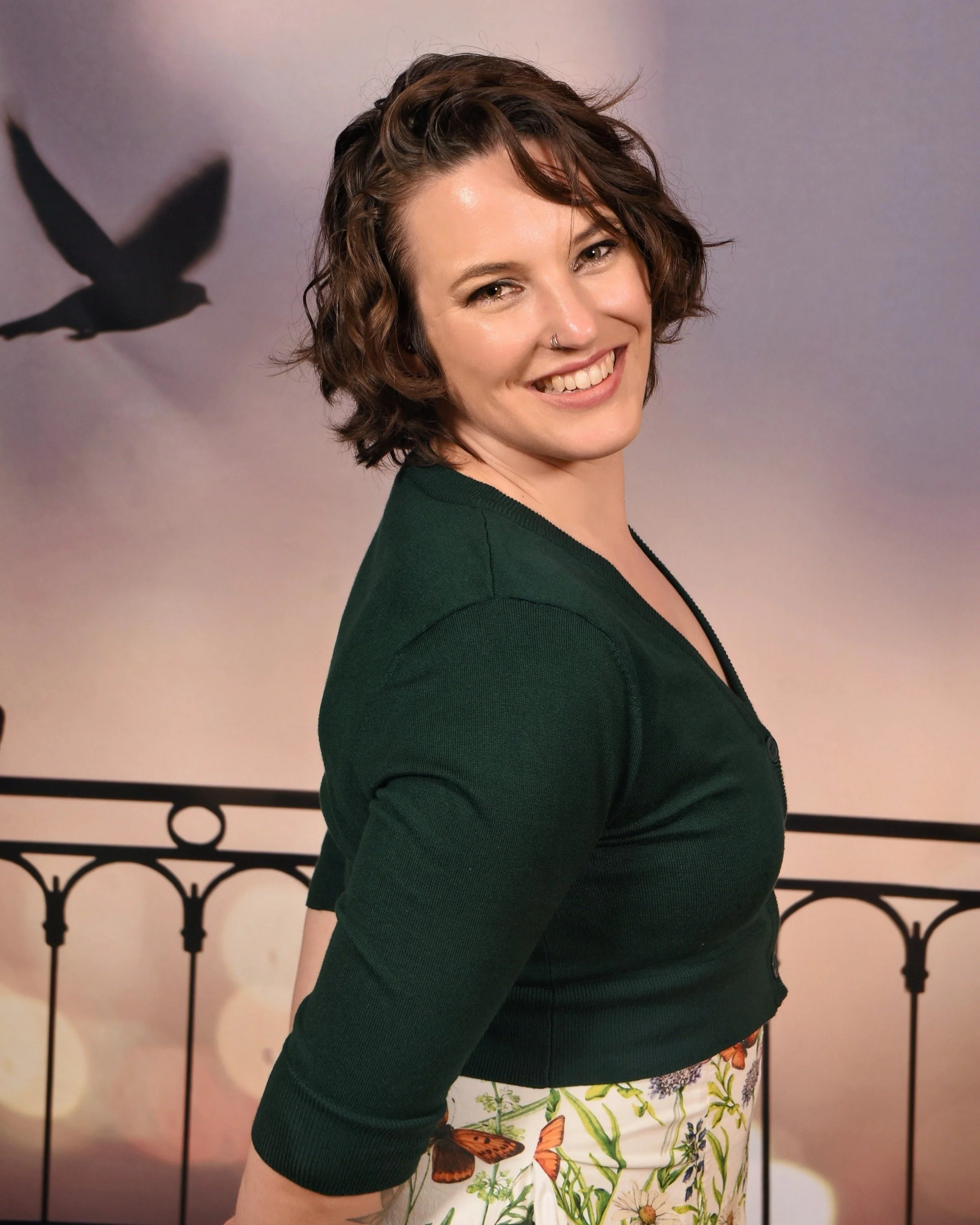 Portrait of Dallas with birds in background. Dallas is wearing a floral dress with an emerald green crop length cardigan.