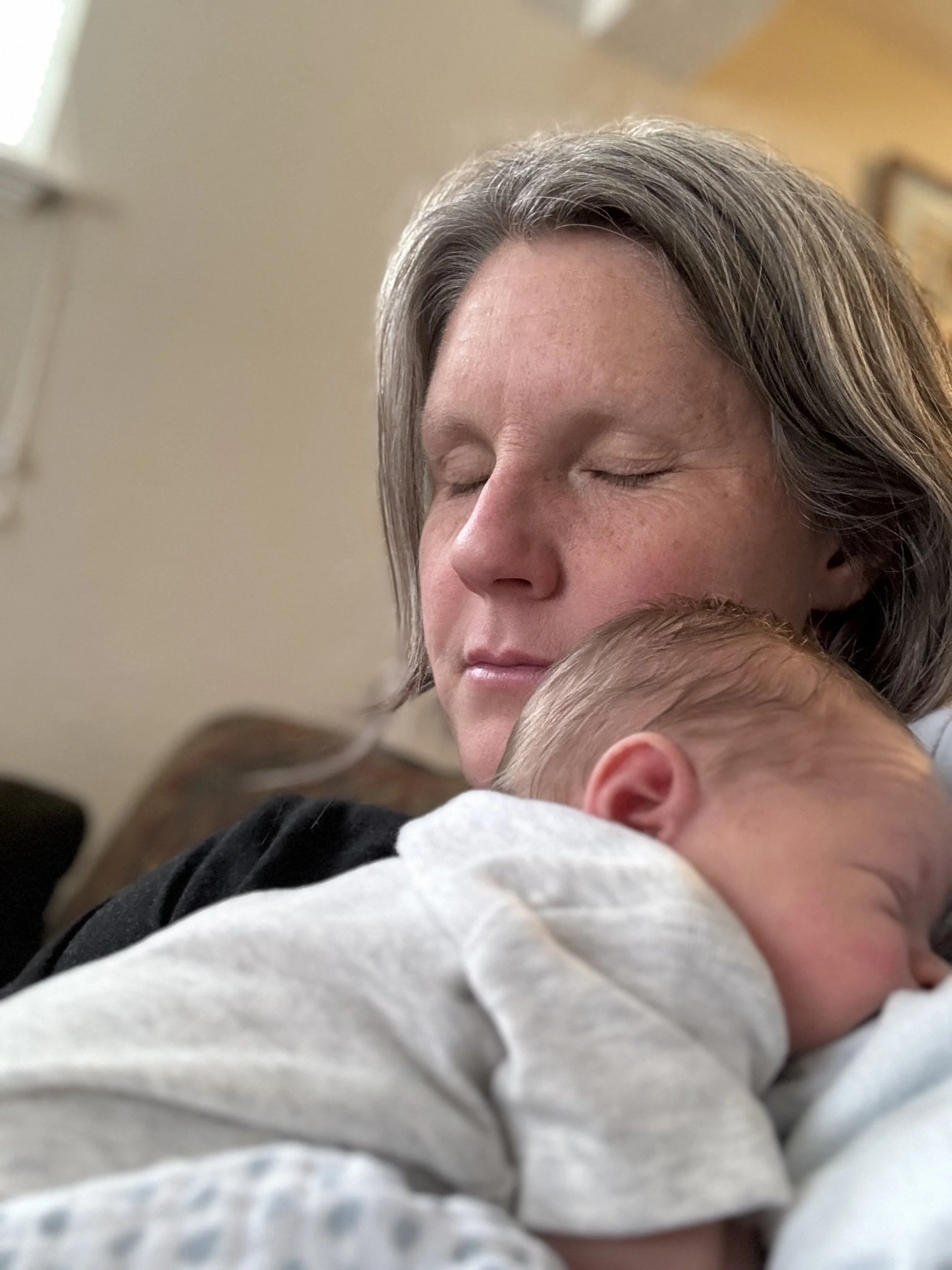 A woman with gray hair and closed eyes holding a sleeping baby