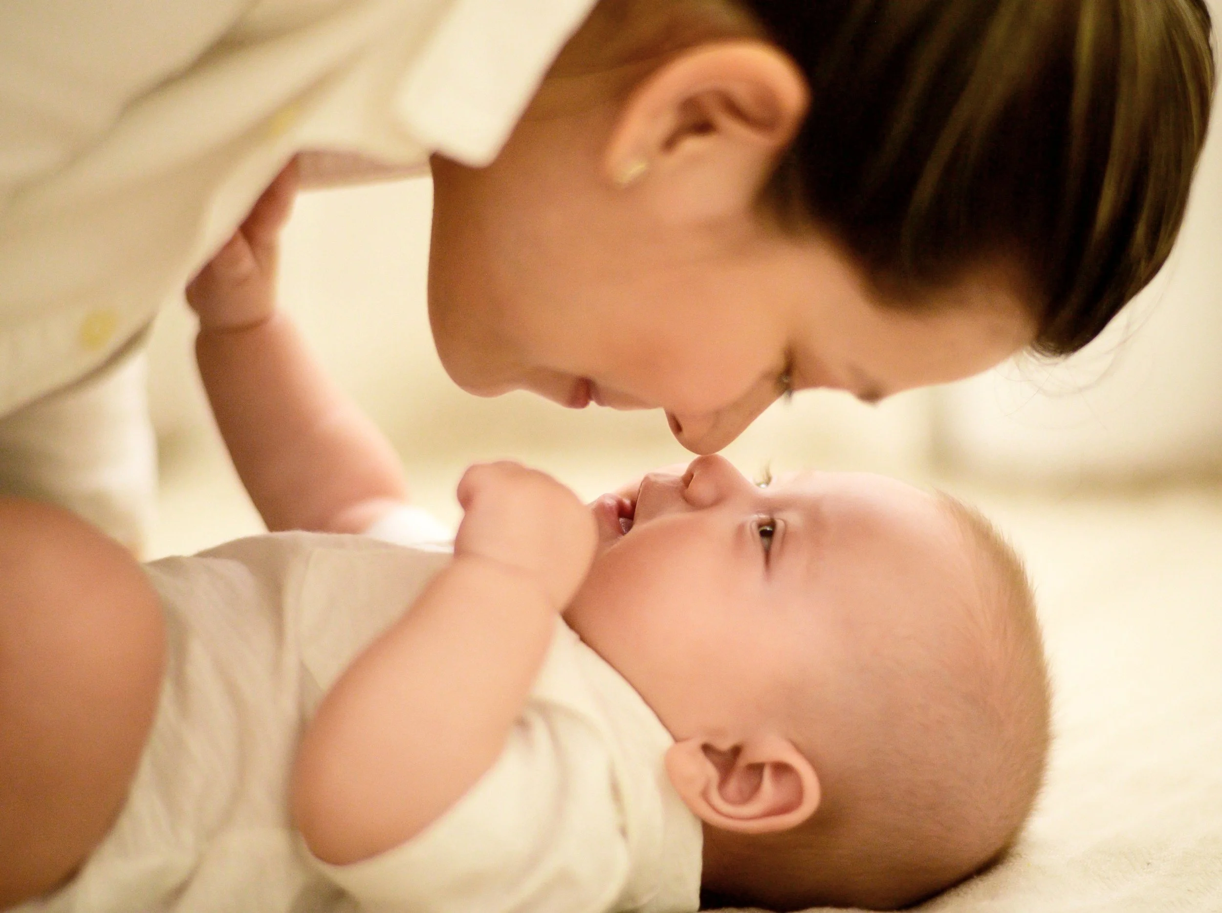 A woman and a baby lying on a bed, facing each other closely, with their foreheads touching and smiling.
