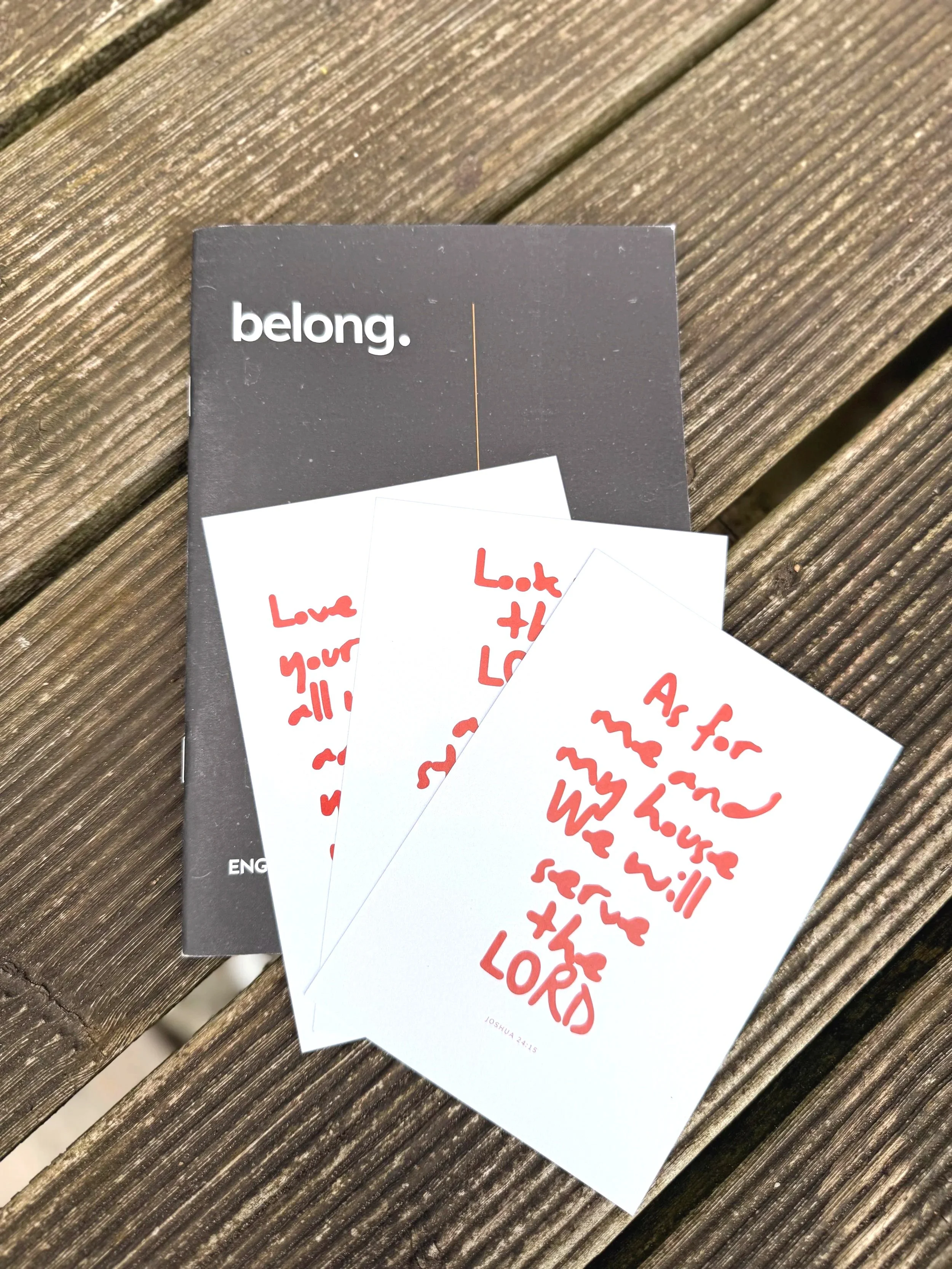 Three white cards with red handwritten messages placed on a black and white box, on a weathered wooden surface. The message on the cards reads, "As for me and my house we will serve the LORD."