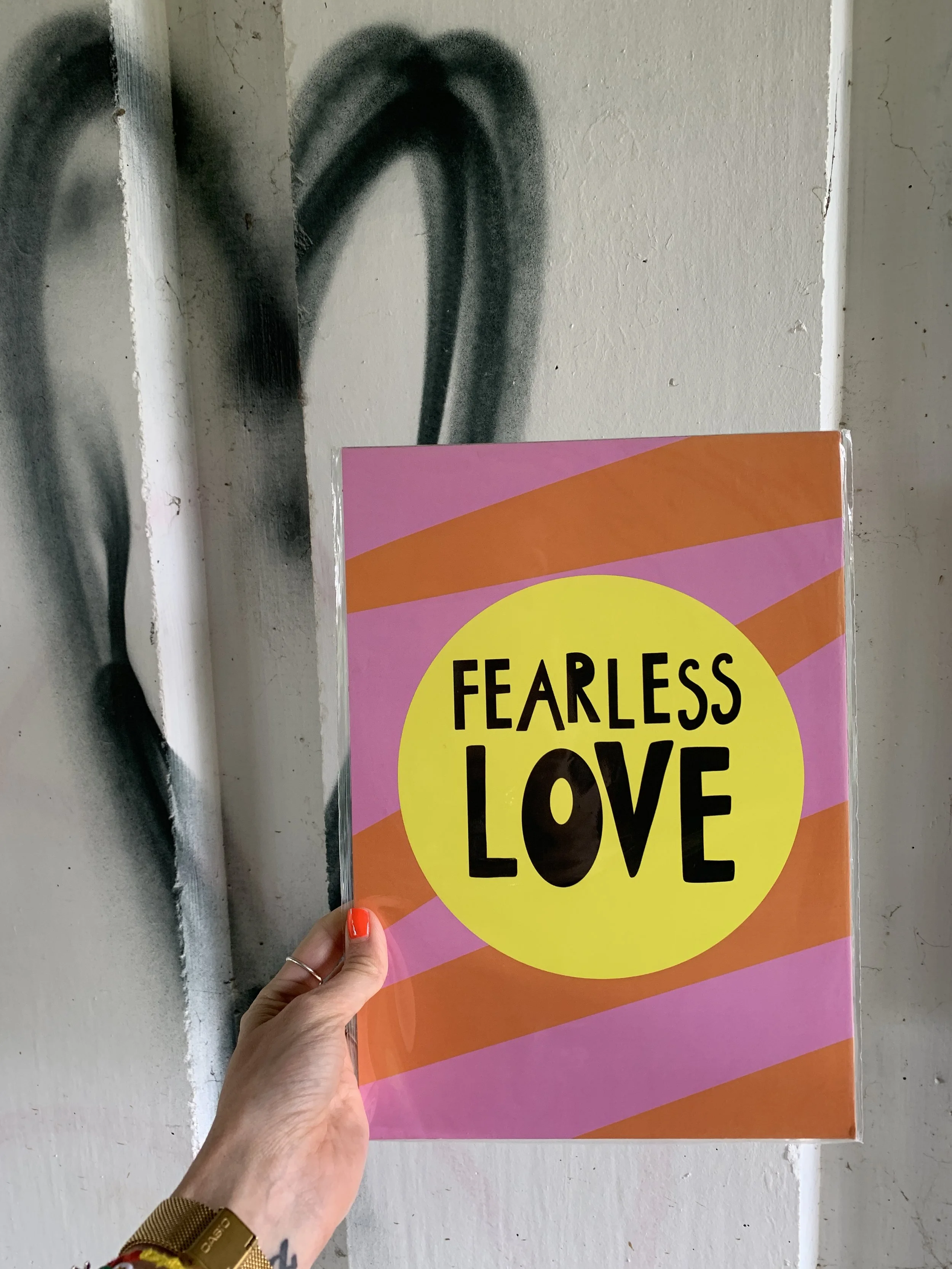 A person holding a colorful book titled 'Fearless Love' with a pink, orange, and yellow cover. The person has red painted nails and is wearing a yellow bracelet.