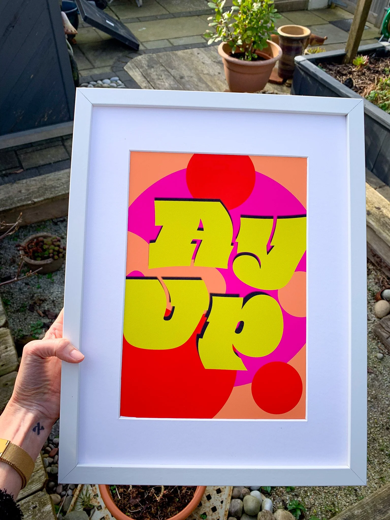 A framed colorful abstract artwork with bold yellow text that appears to spell "AWESOME" on a vibrant pink, red, and orange background with circular shapes.