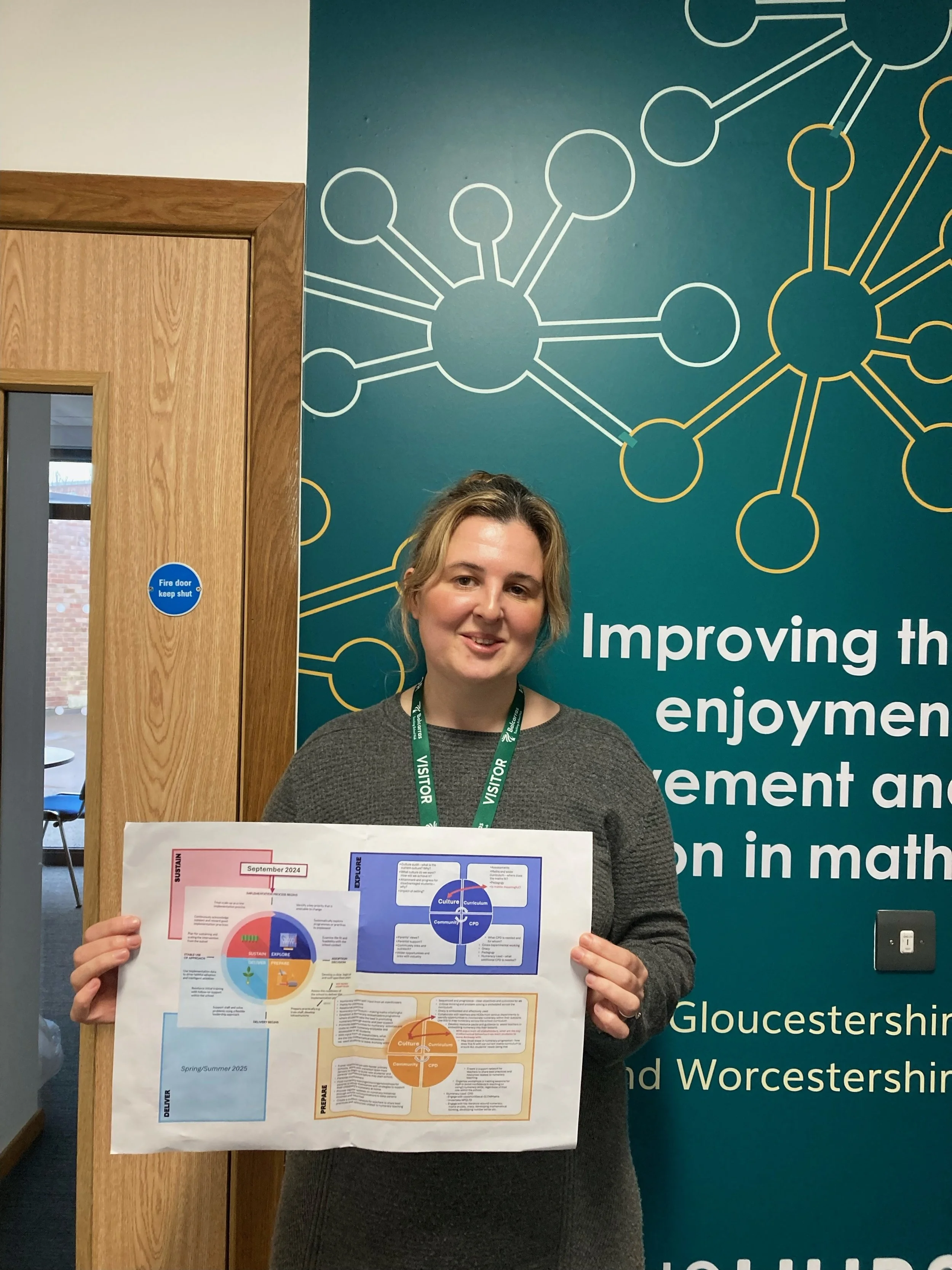A smiling woman holding a colorful infographic poster in front of a blue wall with a network diagram and white text about improving enjoyment and management in mathematics.