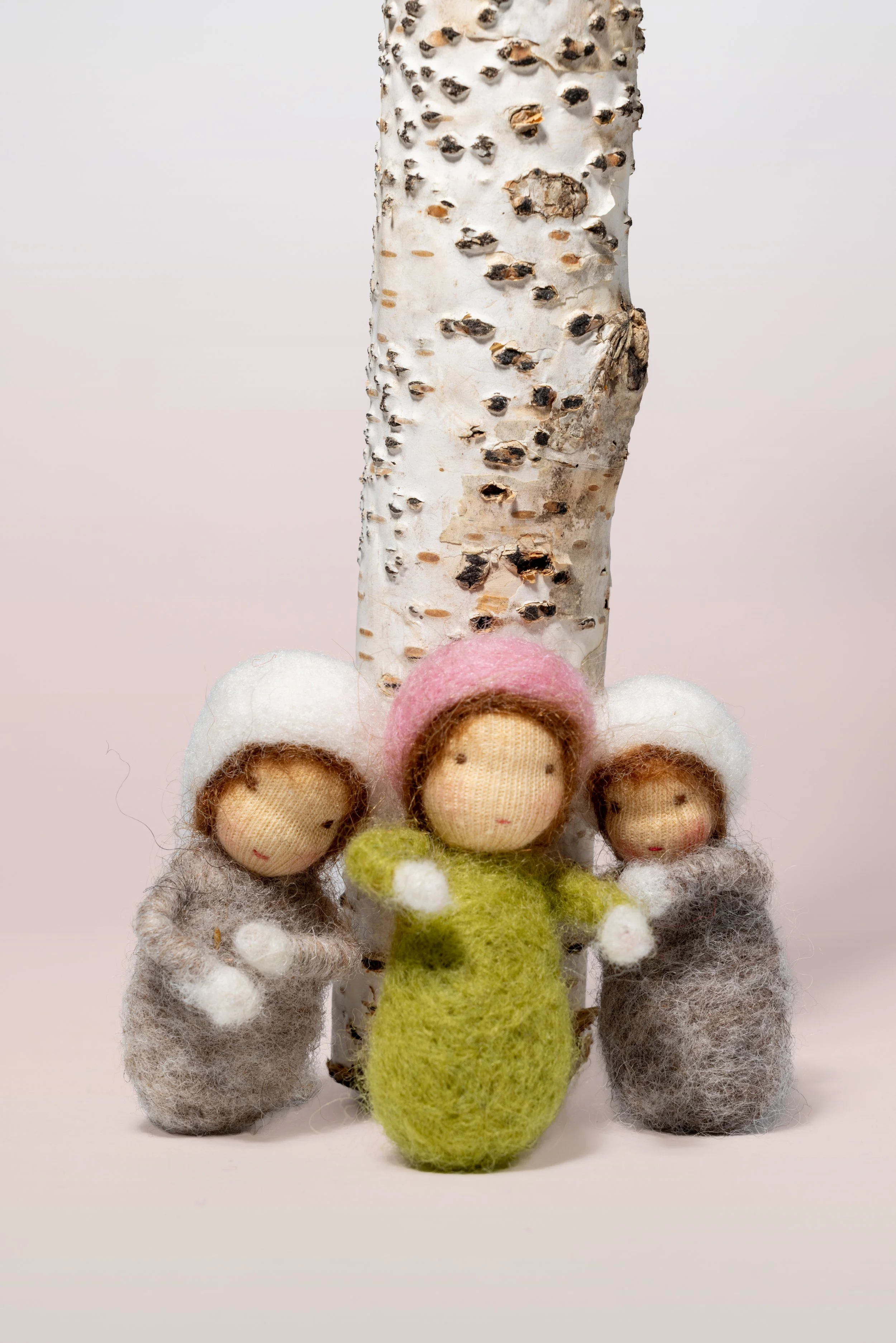 Drei kleine Filzfiguren in Winterkleidung stehen vor einer Birke, Jahreszeitenpüppchen,nach Waldorf-Art.