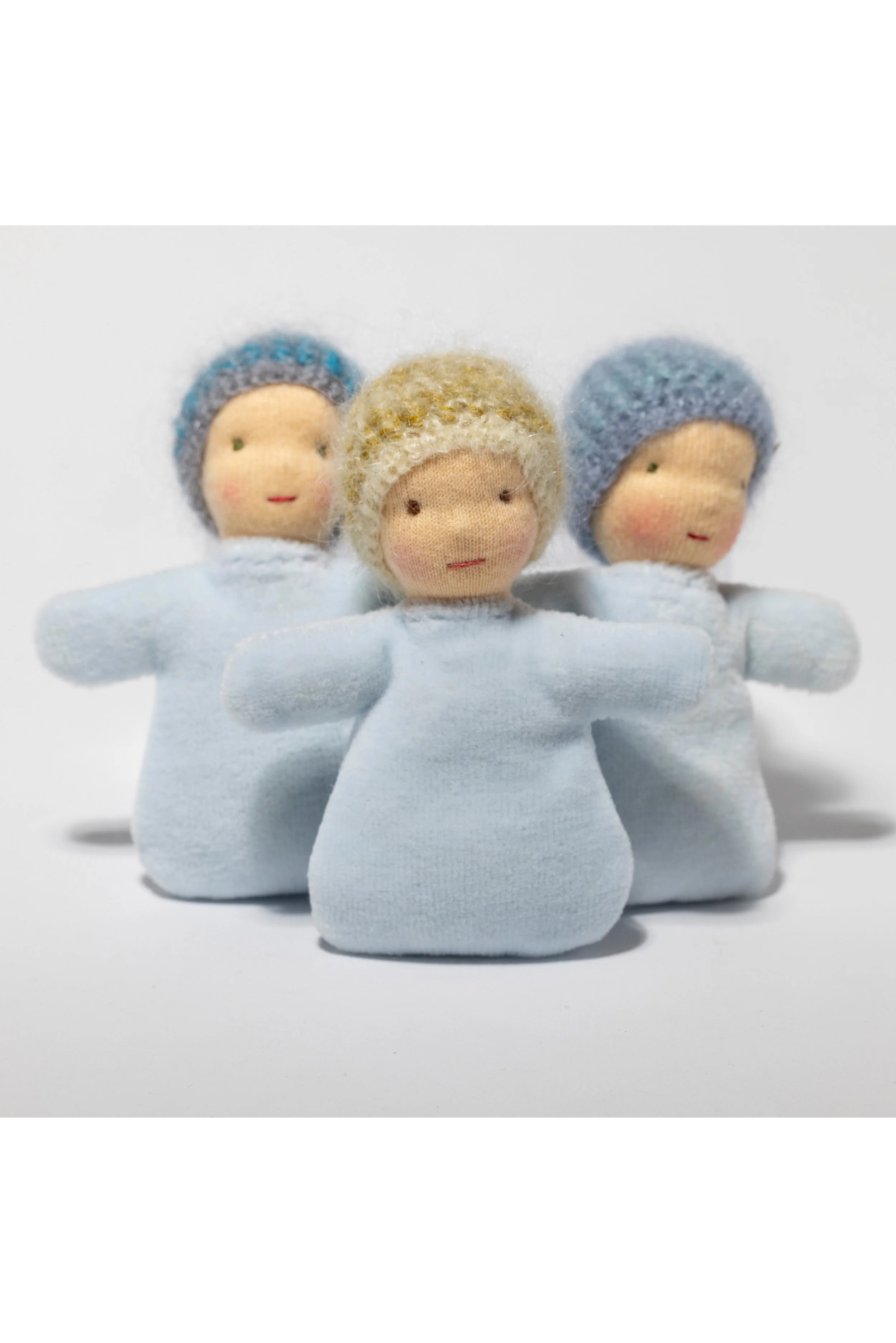 Drei kleine handgefertigte Stoffpuppen in hellblauen Kleidern und bunten Mützen. Waldorf-Art.