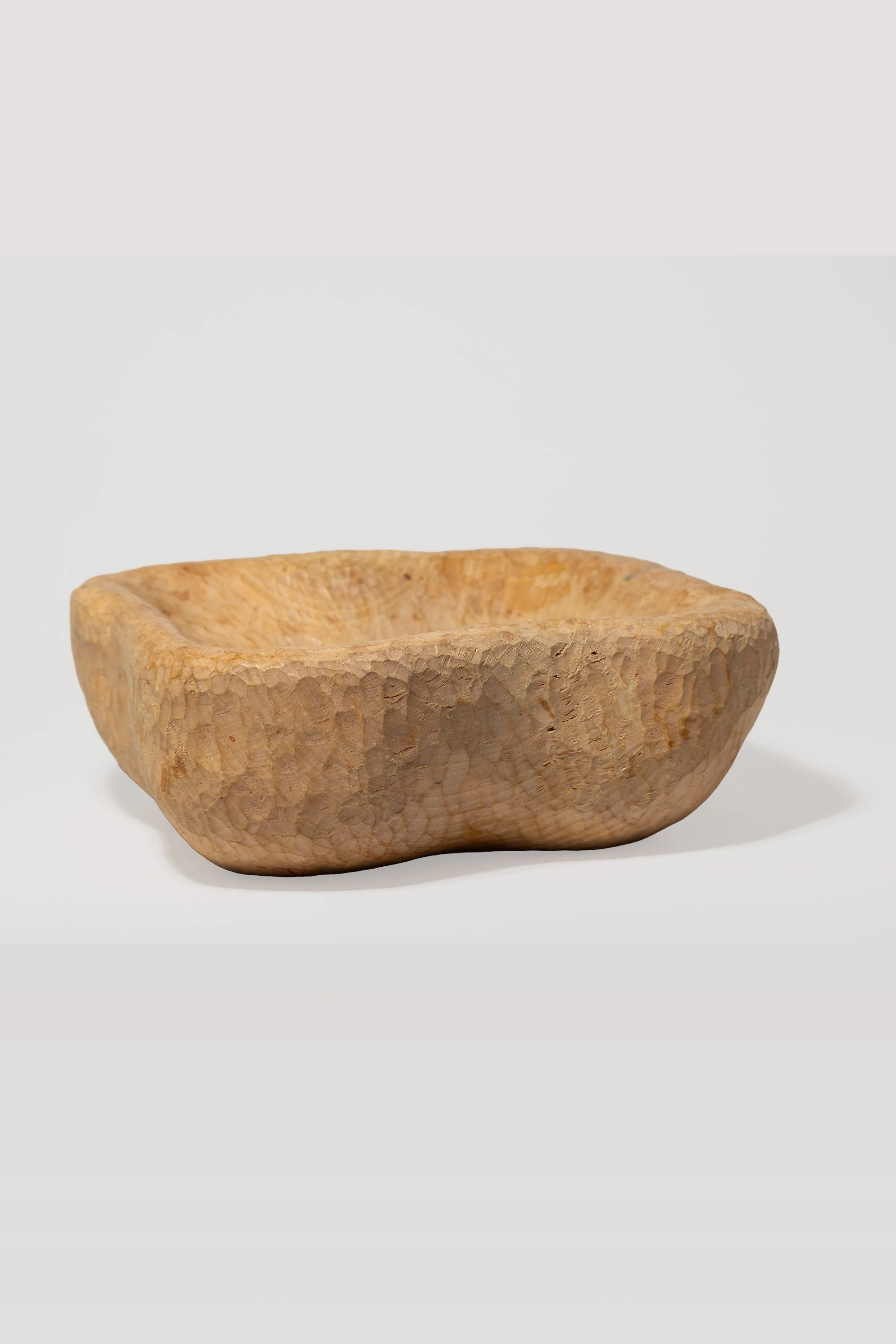 Eine handgeschnitzte Holzschale mit einer rauen, ungleichmäßigen Oberfläche auf weißem Hintergrund.