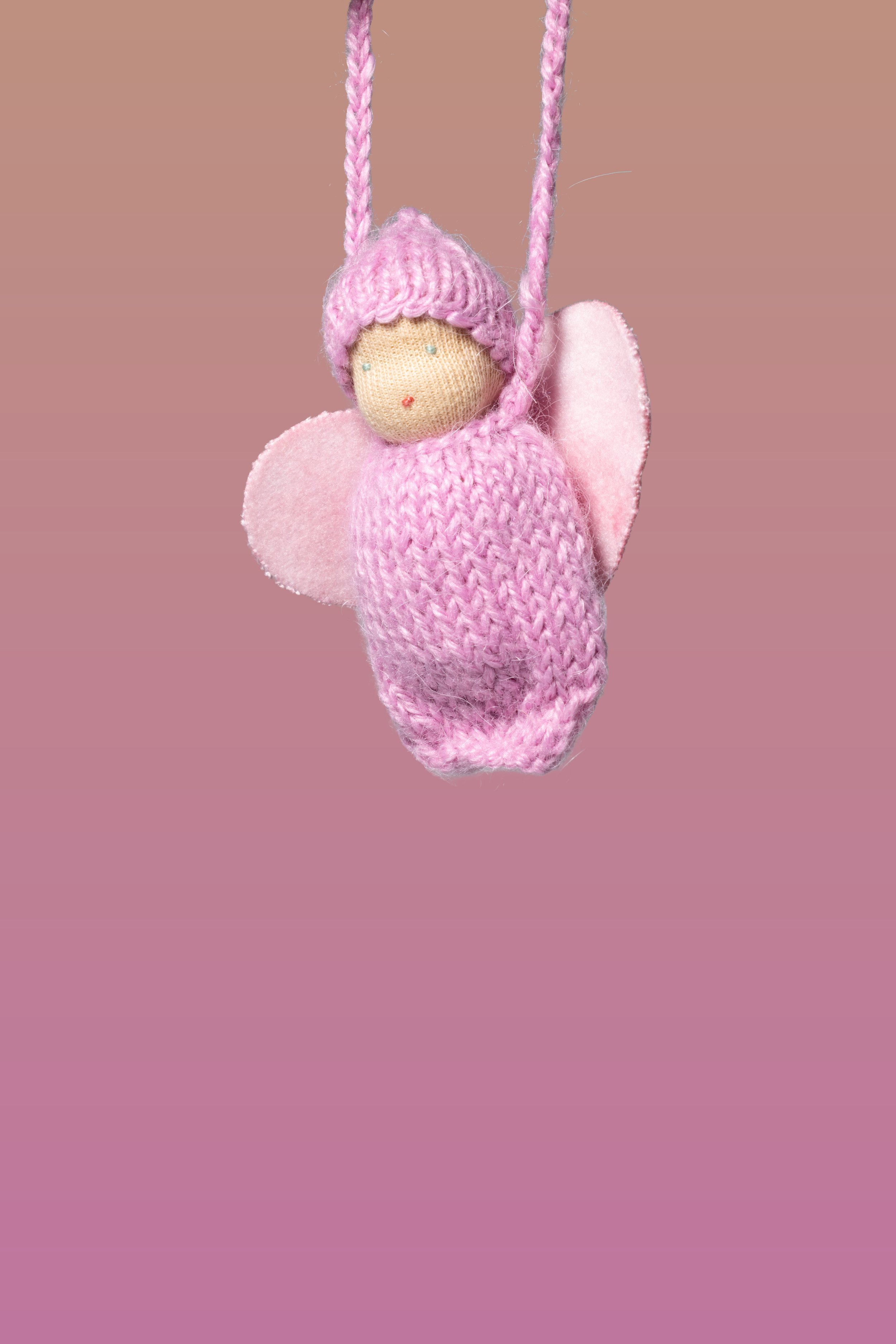 Handgefertigtes Engel-Kunsthandwerk aus Stoff und Wolle, mit rosa Flügeln und Schleife, an rosa Schnur aufgehängt.