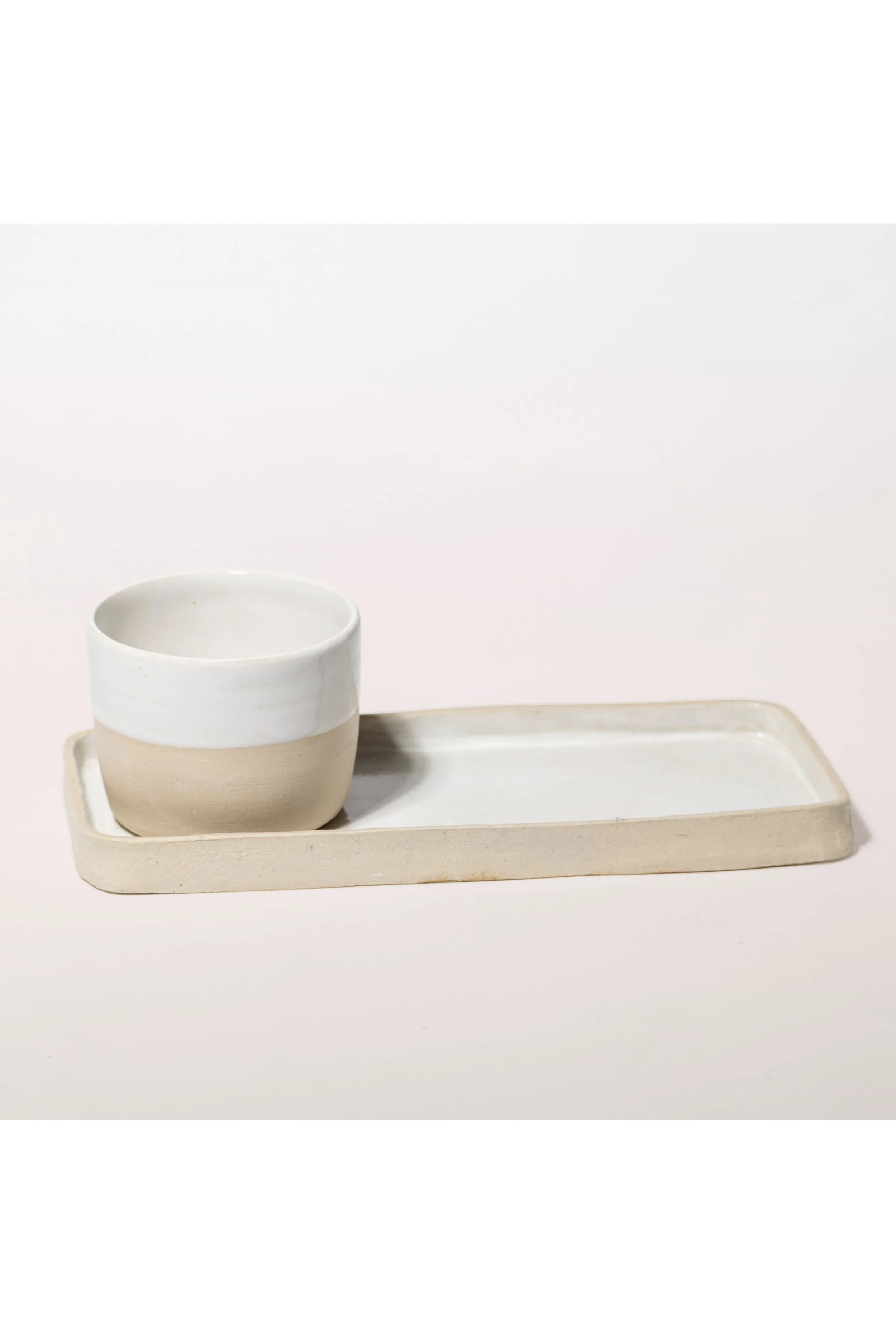 Handgefertigte weisse Tontasse auf einem rechteckigen handgefertigtem Tablett.