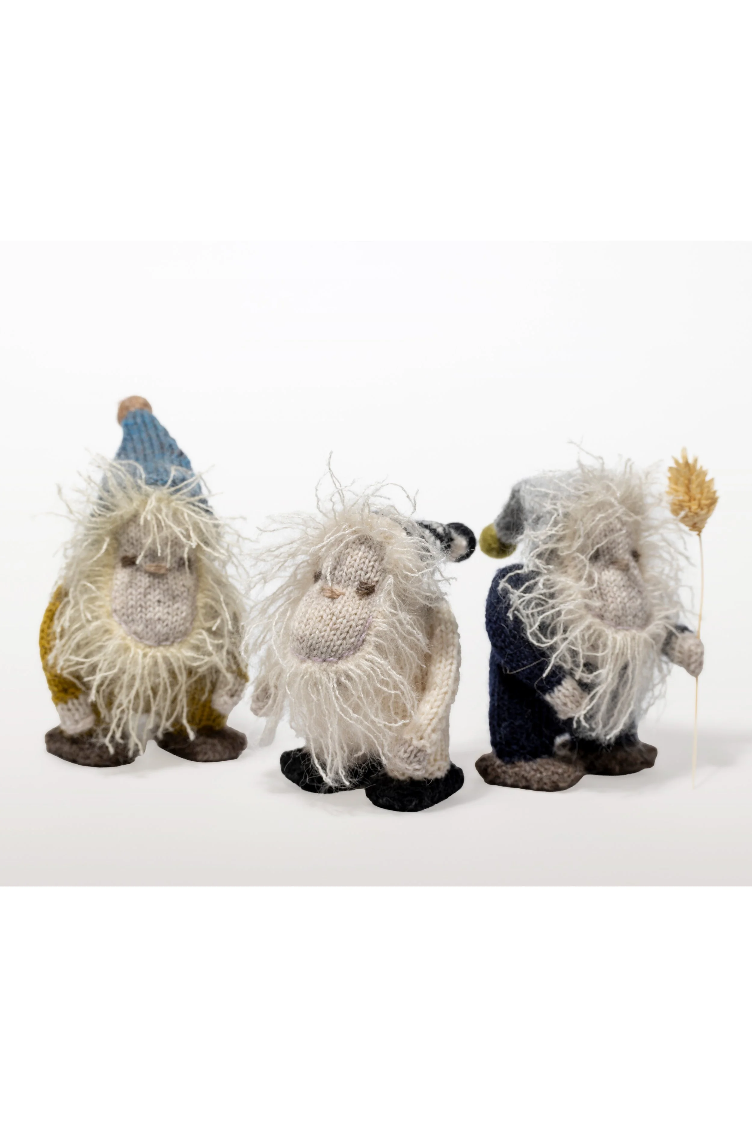 Drei kleine, handgefertigte Figuren, die Zwerge darstellen, mit langen, wuscheligen Haaren und Kleidung, stehen auf einem weißen Hintergrund.