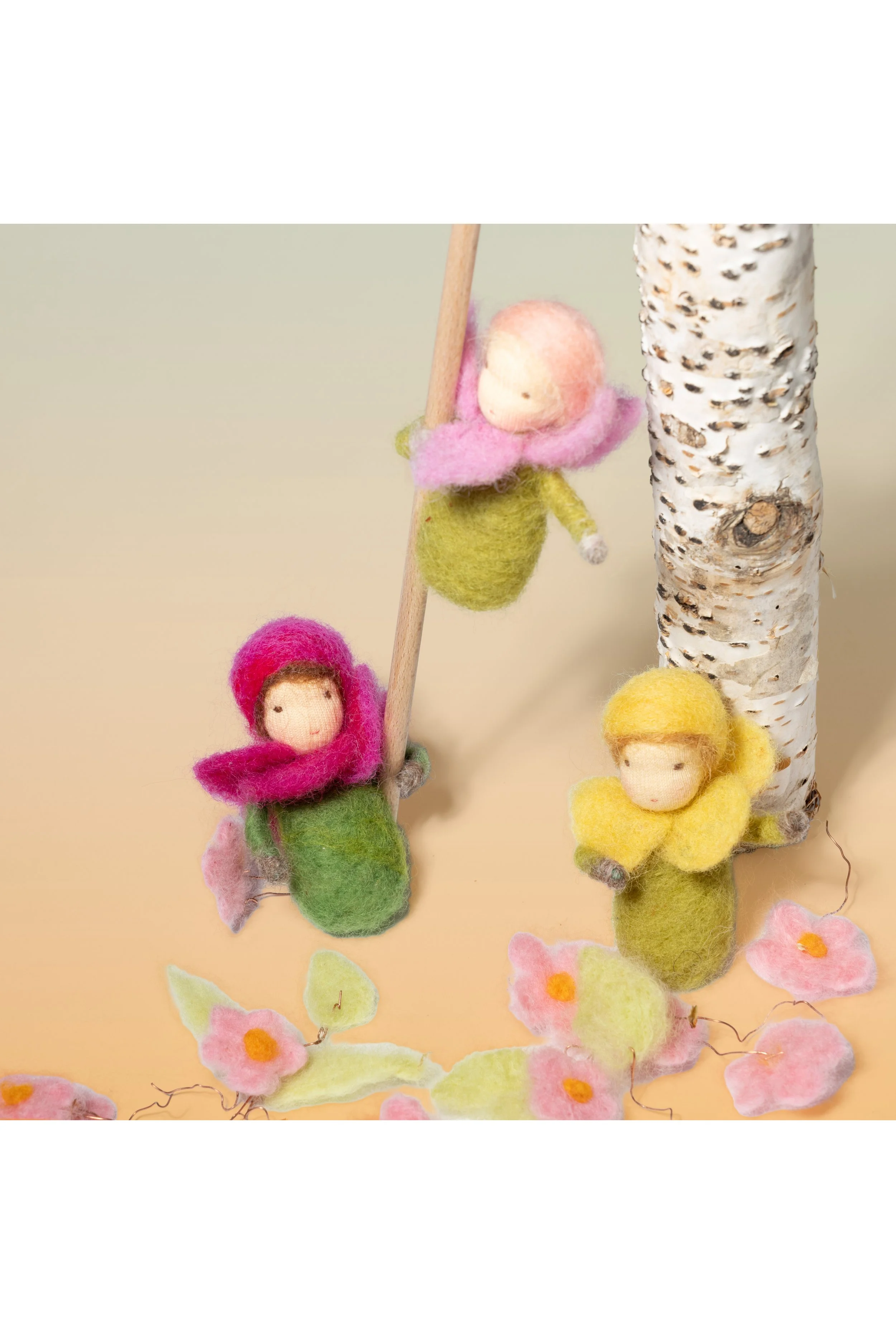 Handgefertigte Filzfiguren Puppchen für den Jahreszeitentisch mit bunten Hauben, die an einem Baum und auf dem Boden sitzen, umgeben von Filzblumen.