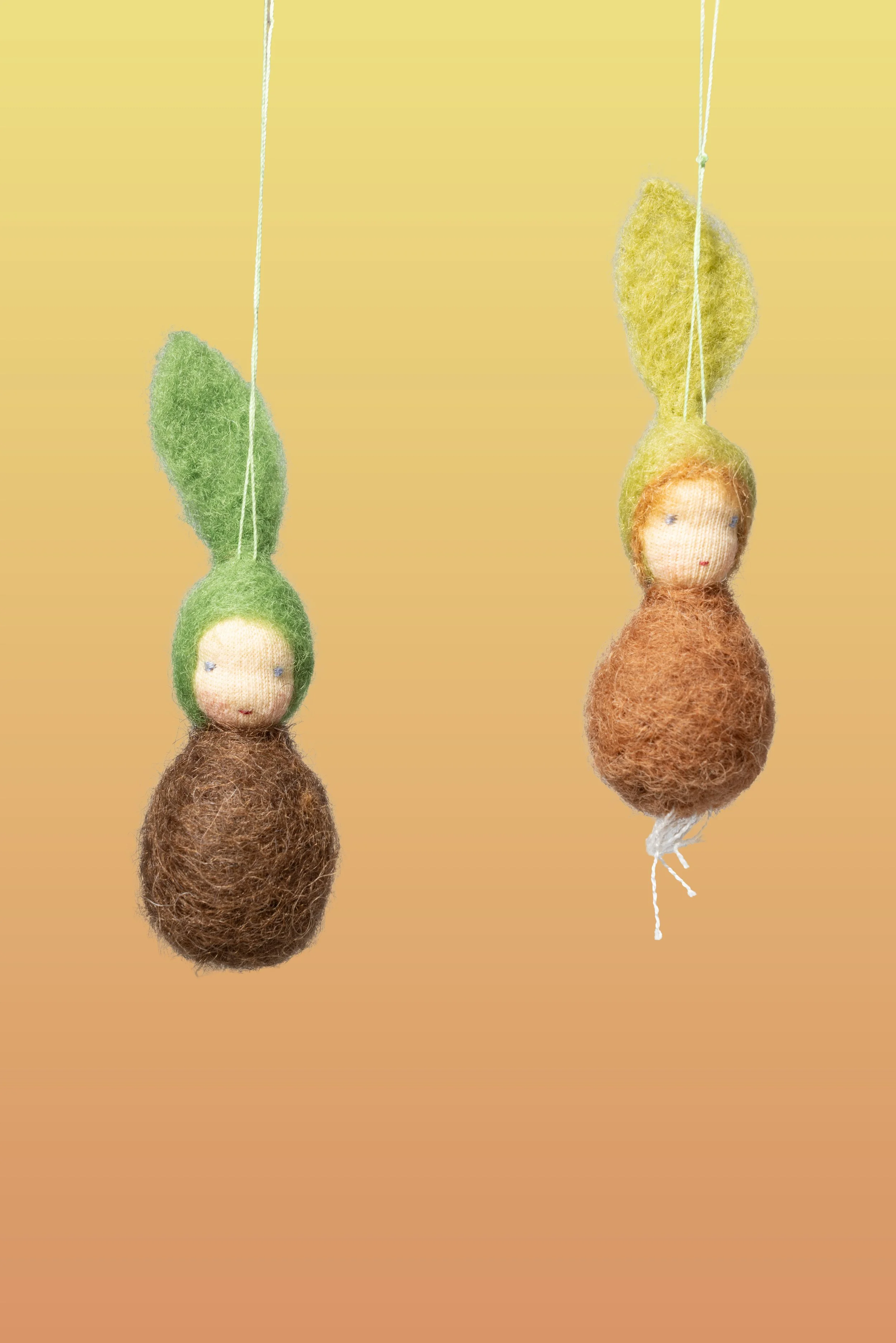 Zwei hängende Dekorationen, die kleinen Wollfigure nmit lustigen, bunten Gesichtern und großen, bunten Hüten in Form von Blättern darstellen, aus Filzstoff gefertigt.