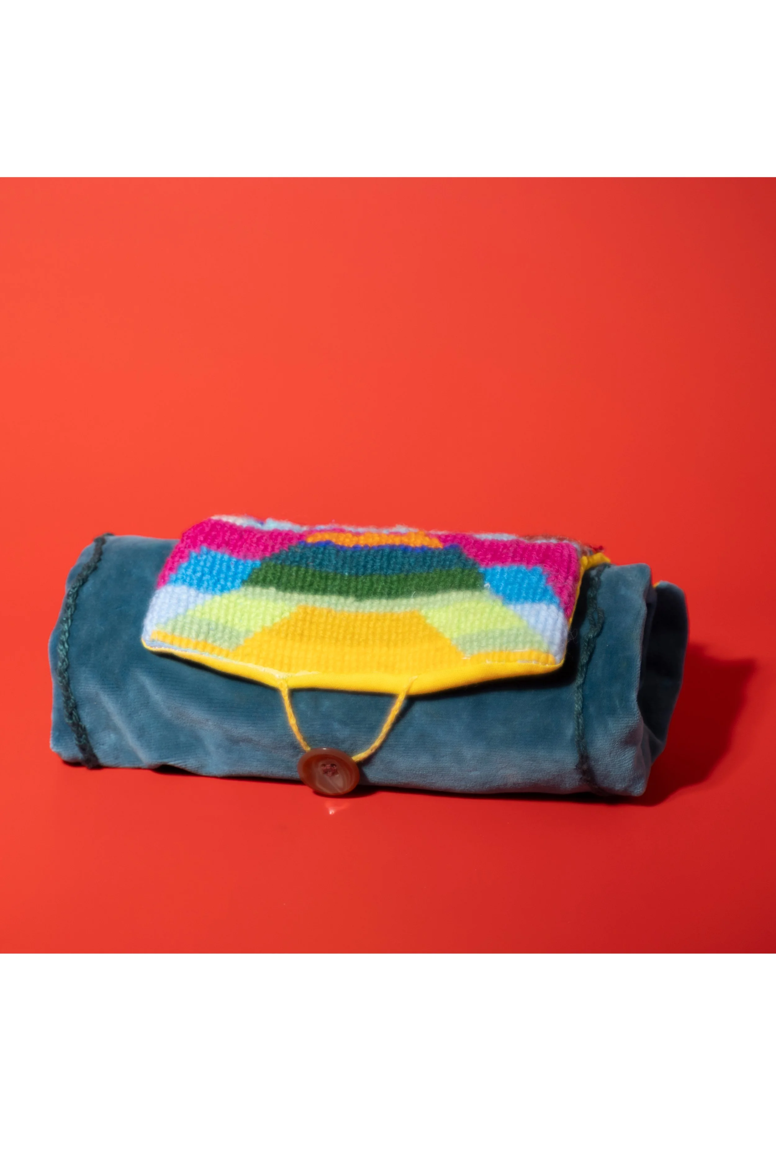Ein zusammengerolltes blauer Stiftemäppchen aus Stoff mit einem bunten, gewebten Stoffstück mit einem geometrischen Muster auf der Oberseite, vor orangefarbenem Hintergrund.