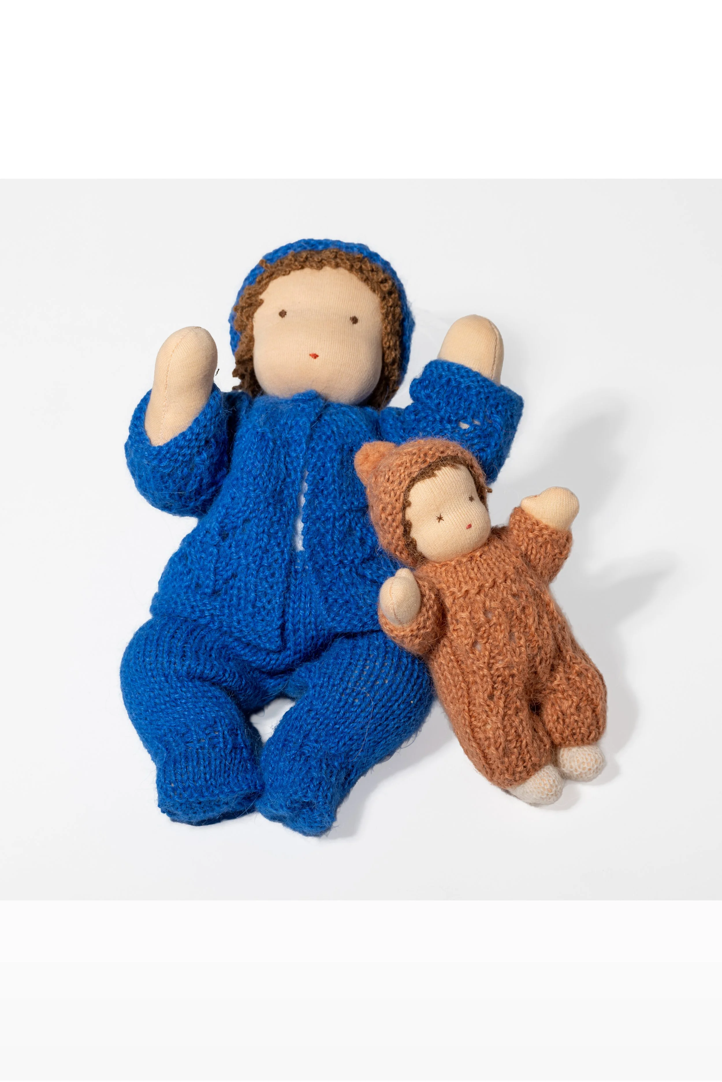 Zwei handgefertigte Stoffpuppen, Waldorf-Art, eine in blauer Kleidung und die andere in brauner Kleidung, liegen auf einem weißen Hintergrund.
