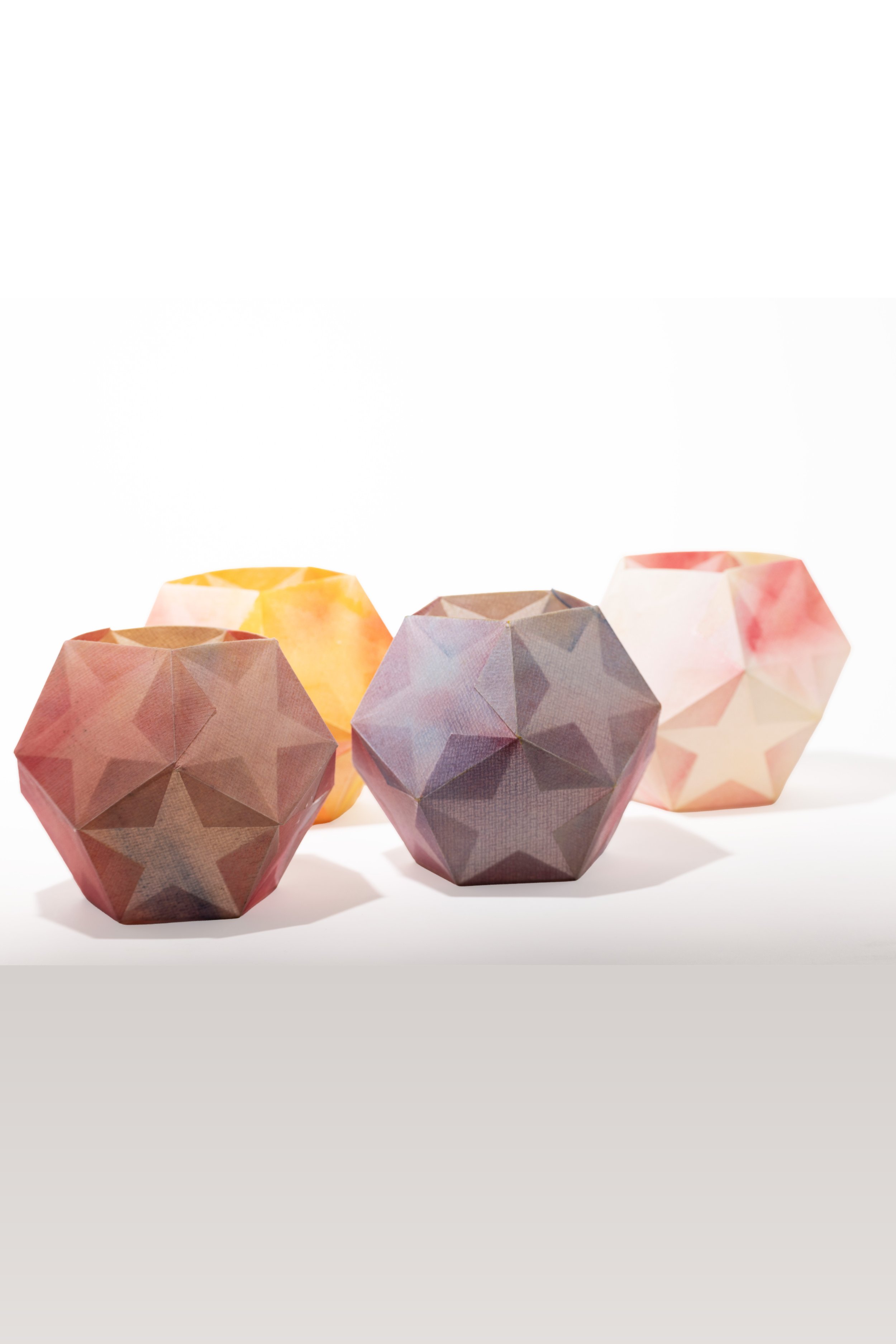 Vier geometrische Lampenschirme mit Sternmuster in Pastellfarben auf weißem Hintergrund.