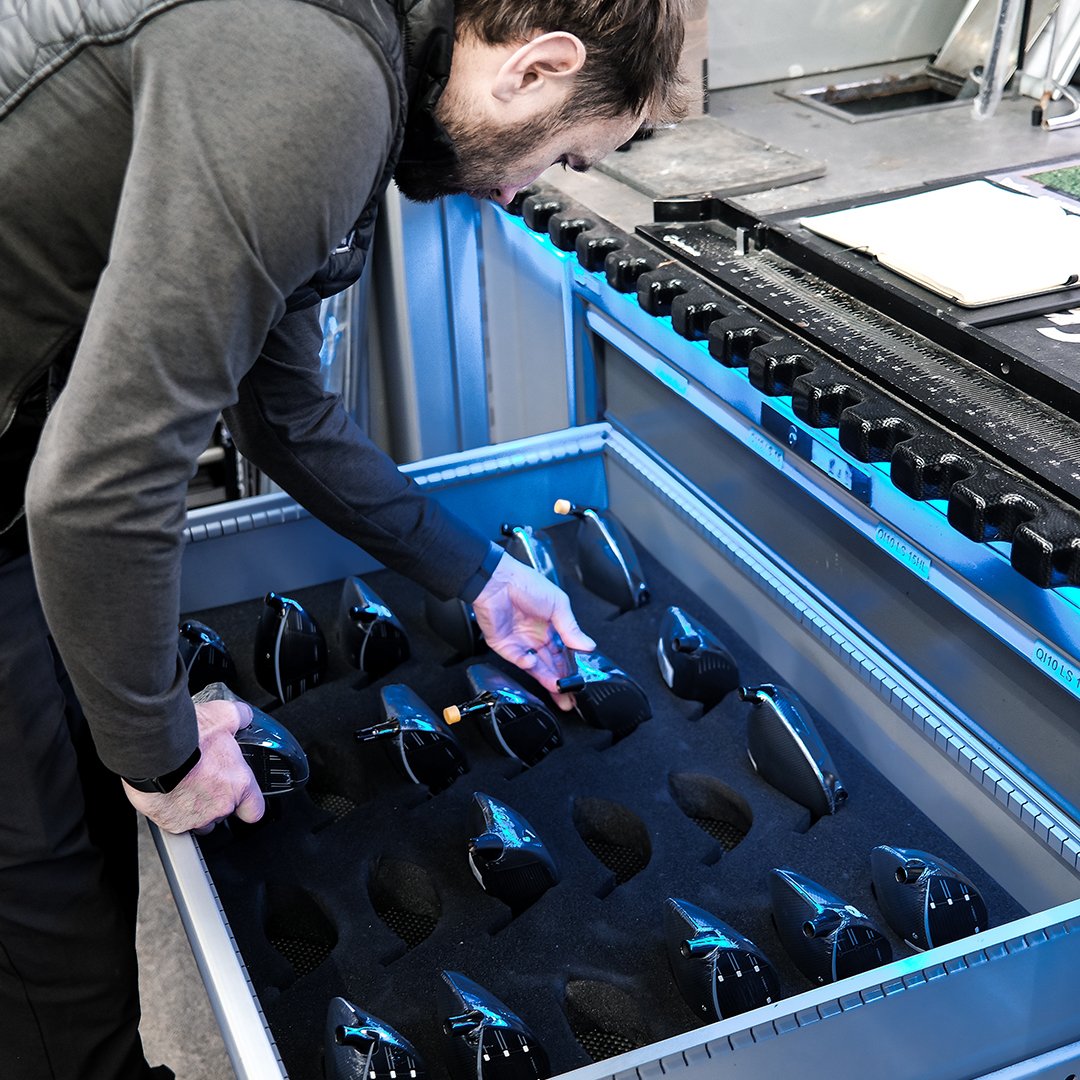 A golfer prepares to tee off on a golf course during daytime with a partly cloudy sky and a crowd of spectators in the background.