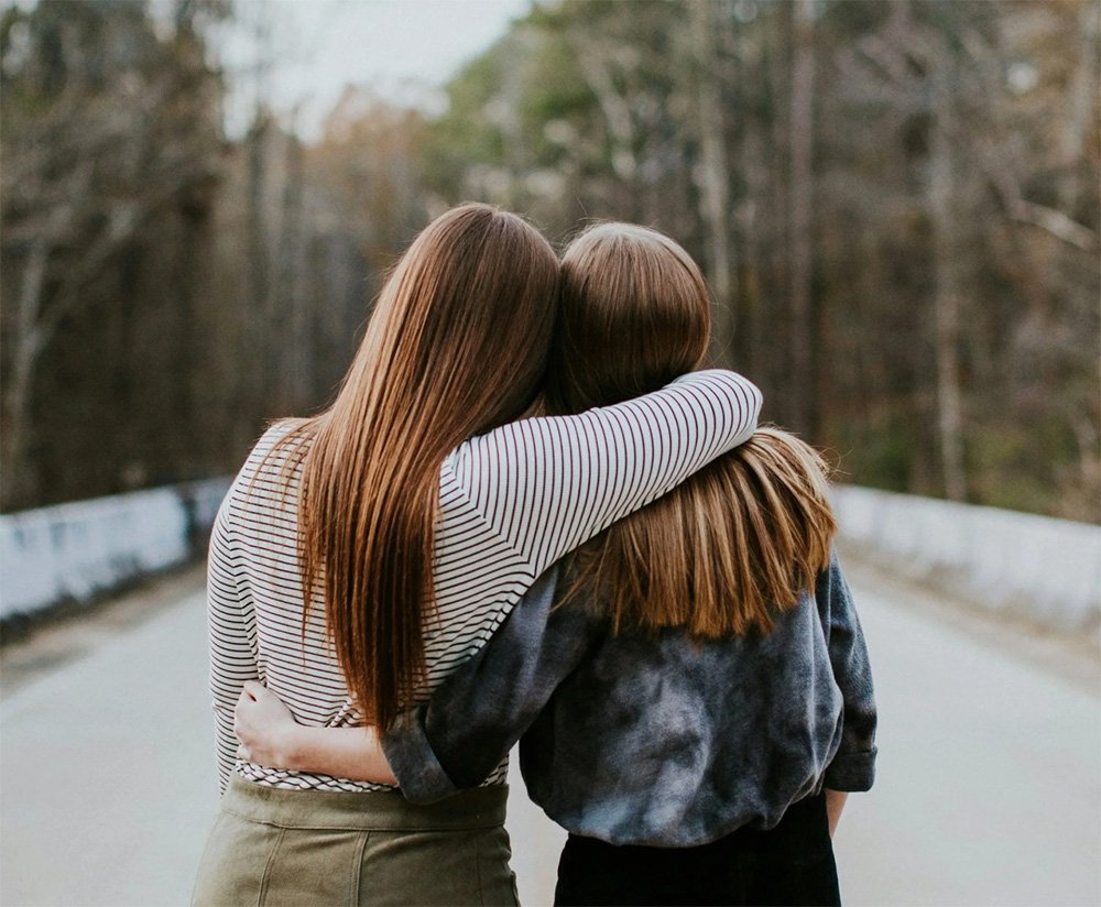 Two women embracing on a road with trees in the background.