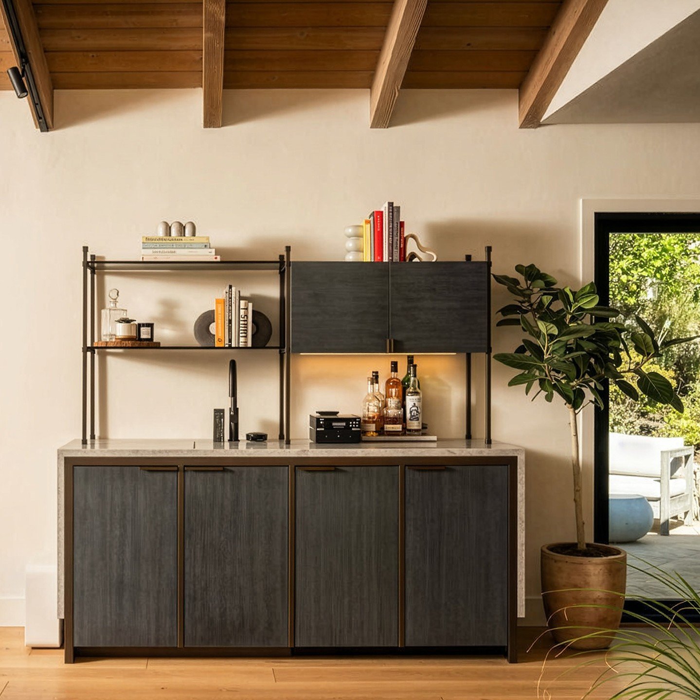 A custom wet bar we designed turns evening cocktails into an effortless ritual. Its doors are finished in moody blue-stained oak and trimmed in oil-rubbed bronze; the interior of the upper cabinet is lined with smoked mirror, adding a quiet glamour t