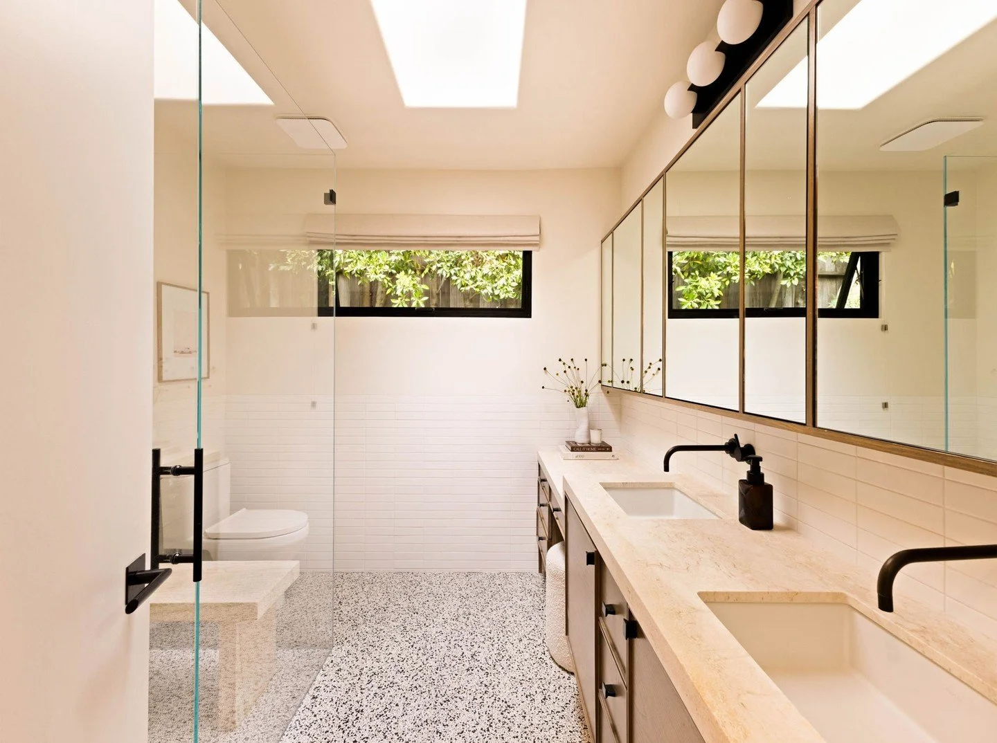 A primary bathroom, where clean lines and beautiful finishes come together to create a modern spa-like retreat. We designed a wall-to-wall medicine cabinet provides ample storage, while a floating walnut vanity includes a lower counter dedicated to m