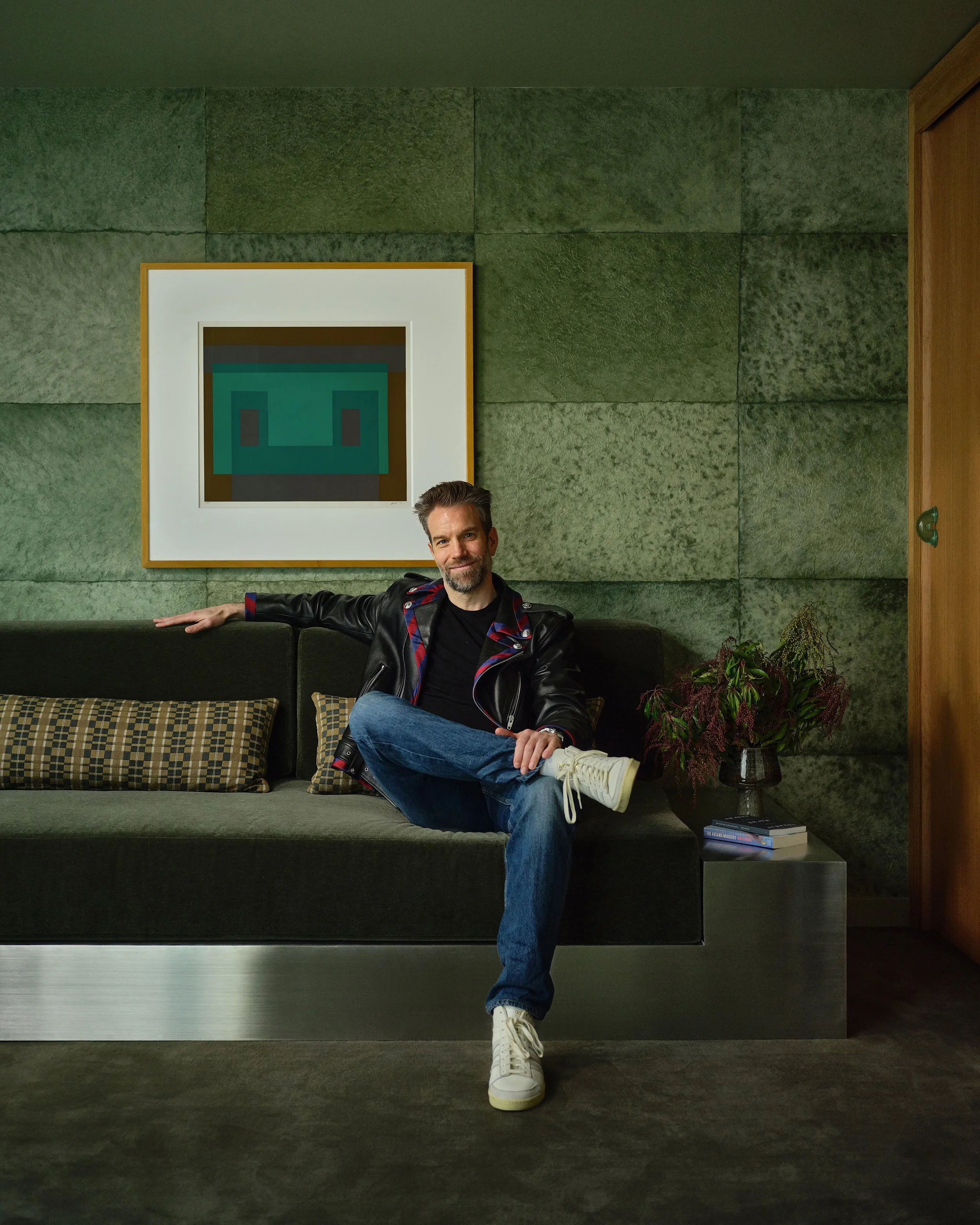 Comedian Anthony Jeselnik's home by Riccio Vidaurre Design.  A monochromatic teal green room with cannon bullock wallpaper, a green rug, a stainless steel and mohair sofa and a painting by Joseph Albers.