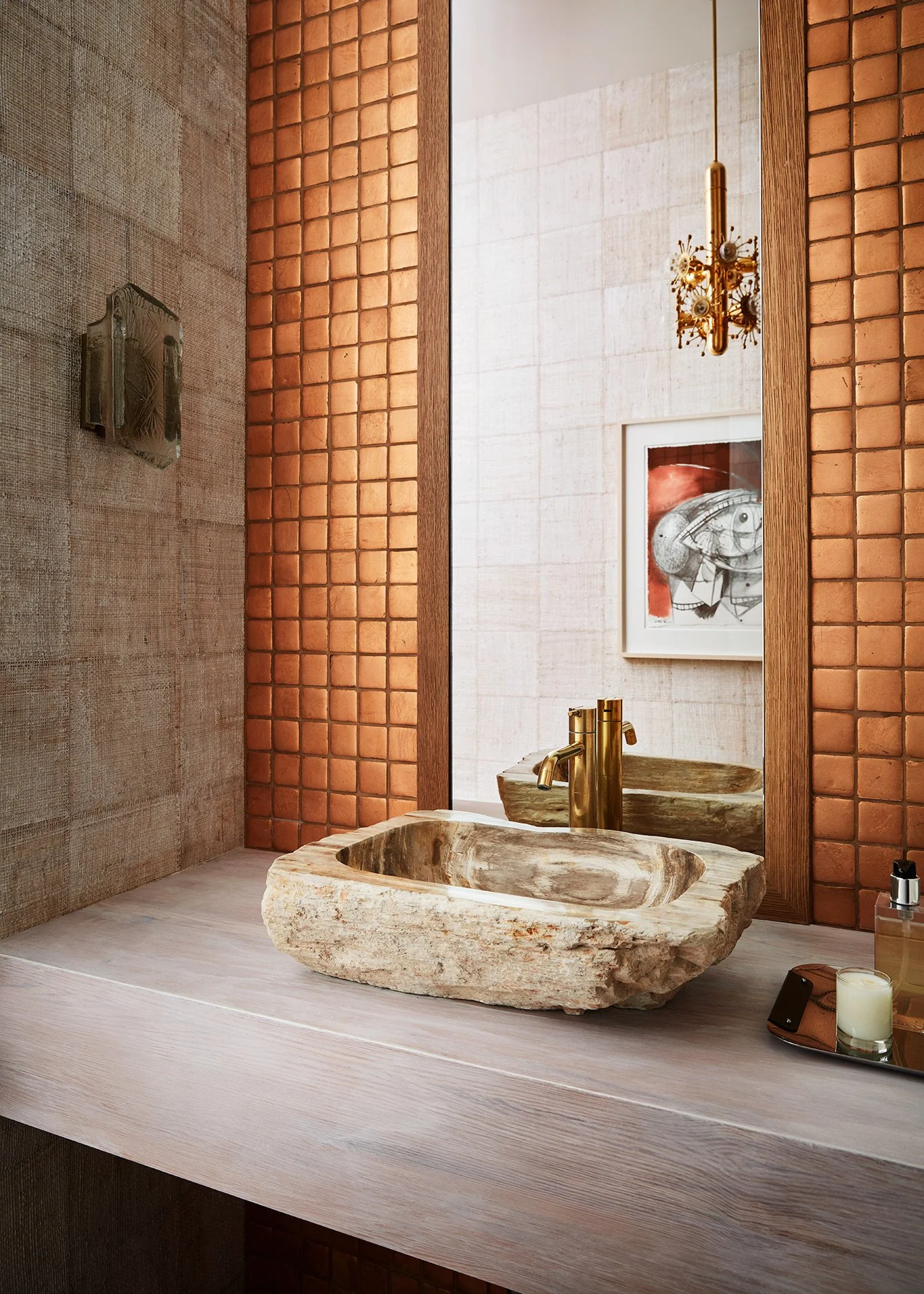 Bathroom with a rustic stone sink, gold faucet, large mirror, framed artwork, and textured walls.