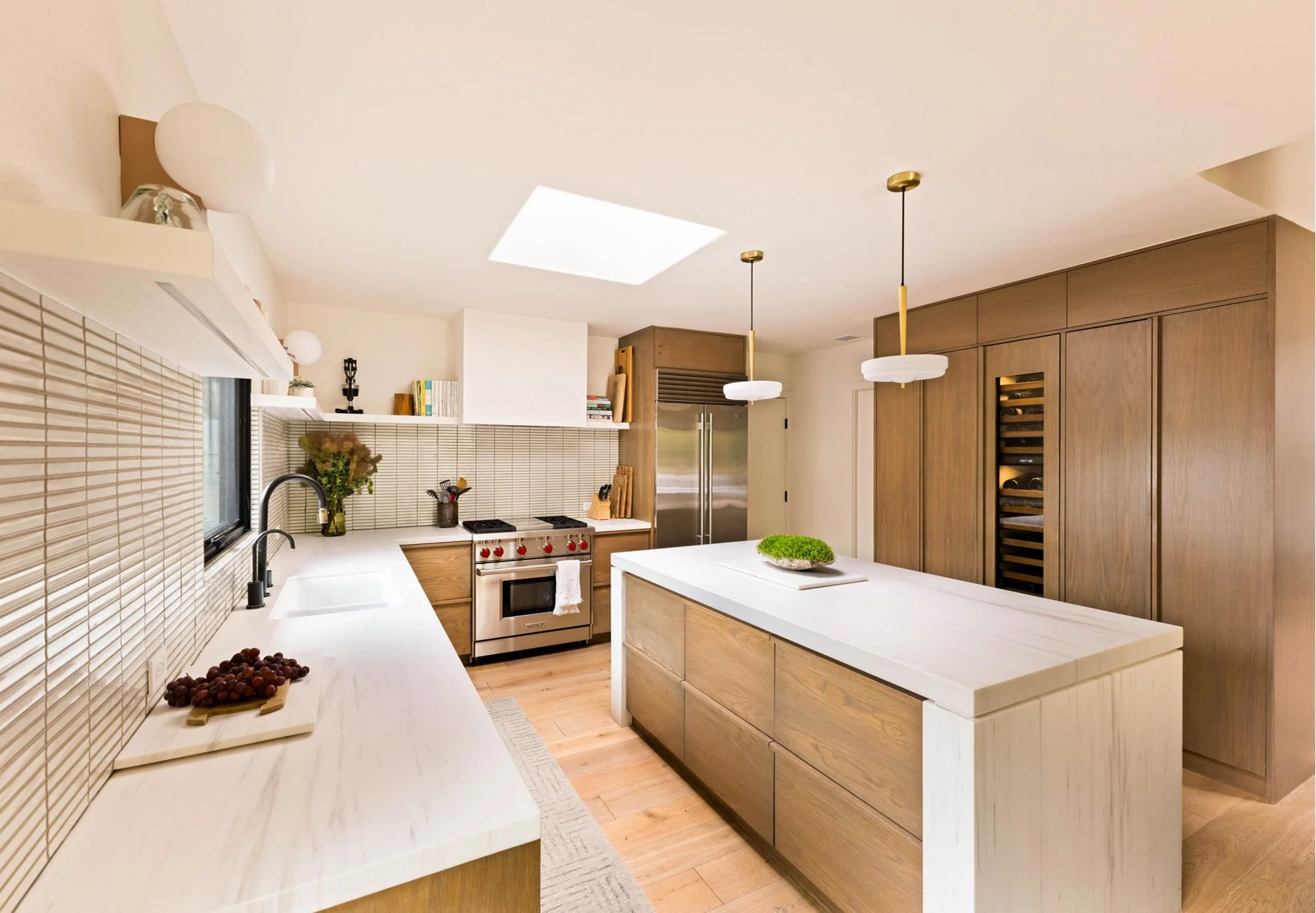 A modern kitchen with white marble island and walnut cabinetry.  Two pendants hang about the island.  Full height cabinets house a wine fridge and a coffee bar.