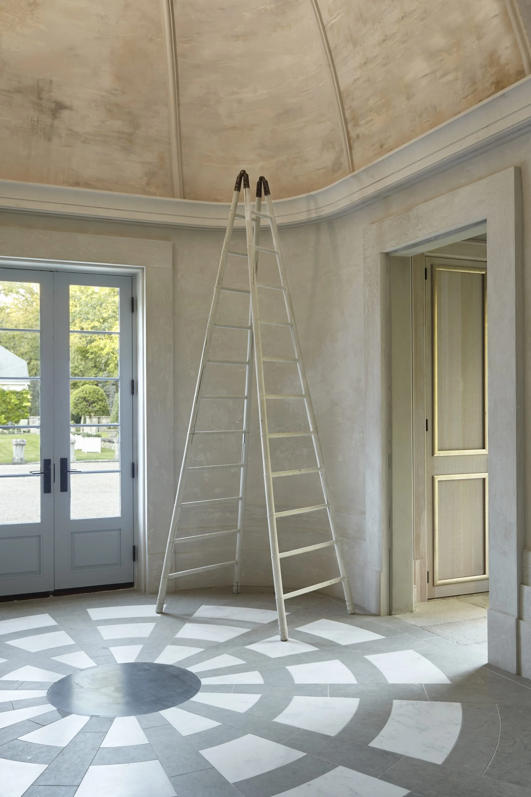Interior room with a white stepped ladder under the ceiling, a set of double glass doors to the outside, and a light-colored patterned floor.