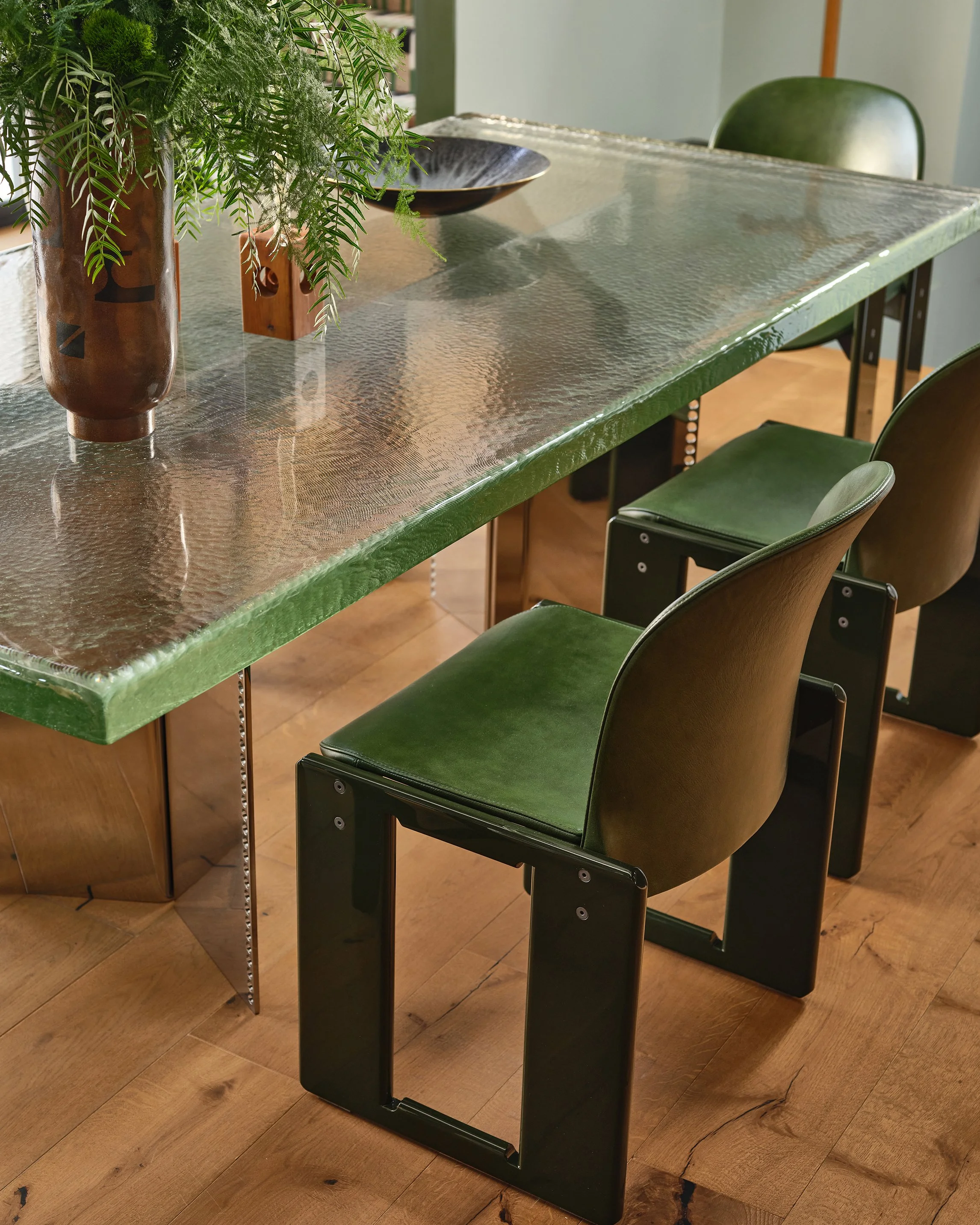 Comedian Anthony Jeselnik’s home – a cast glass dining table by EJR Barnes with green dialogo dining chairs by Tobia Scarpa styled with a ceramic vase with greenery.  Interior design by Riccio Vidaurre Design.