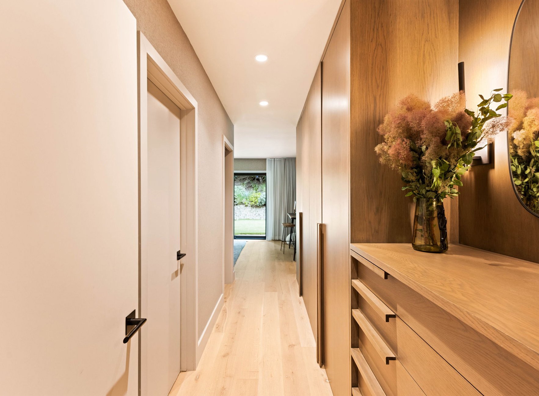 A custom walnut closet in a mid century modern remodeled home.  The built-in dresser has integrated wood pulls with sconces, a mirror and a vase of flowers above.